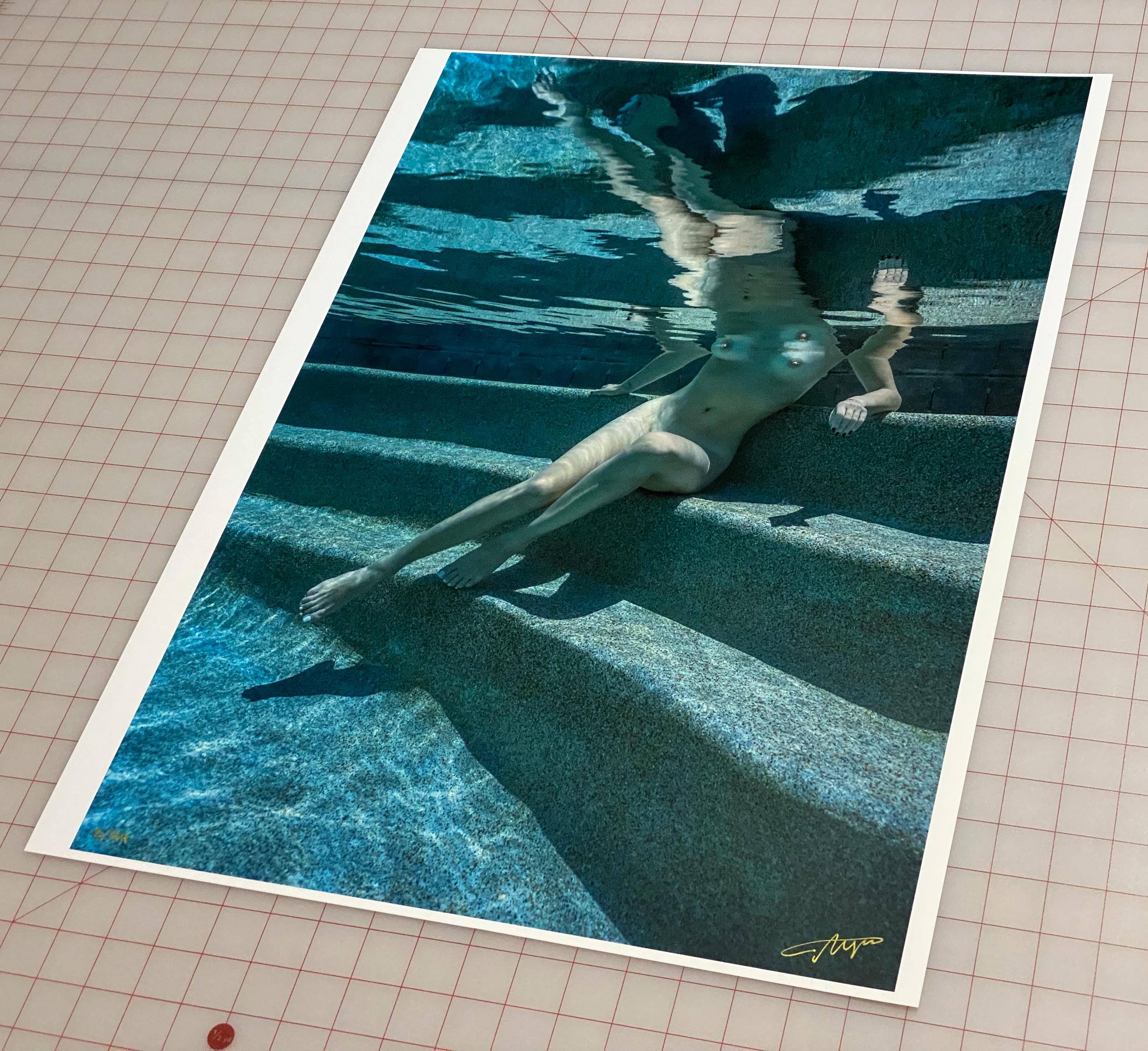 An underwater photograph of a naked young woman sitting on pool steps.  

Original gallery quality print signed by the artist. 
Digital archival pigment print on archival paper with metallic finish. 
Limited edition of 24
Paper size: 36