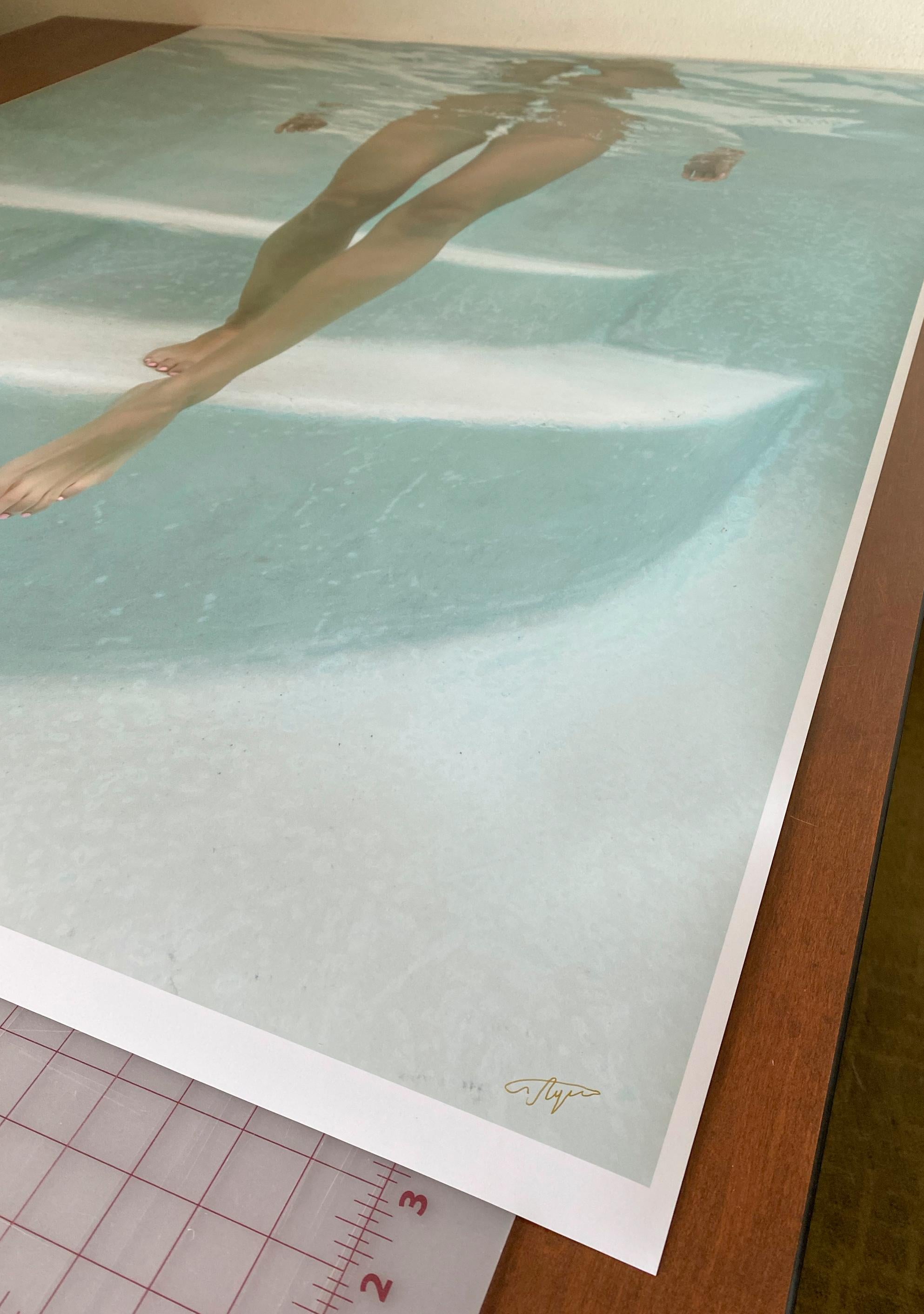 A light and very becoming underwater photograph of a girl walking down the steps in pool toward you. The light blue photograph shows no swimsuit neither any places where you would expect a swimsuit. This photograph gets a lot of attention at