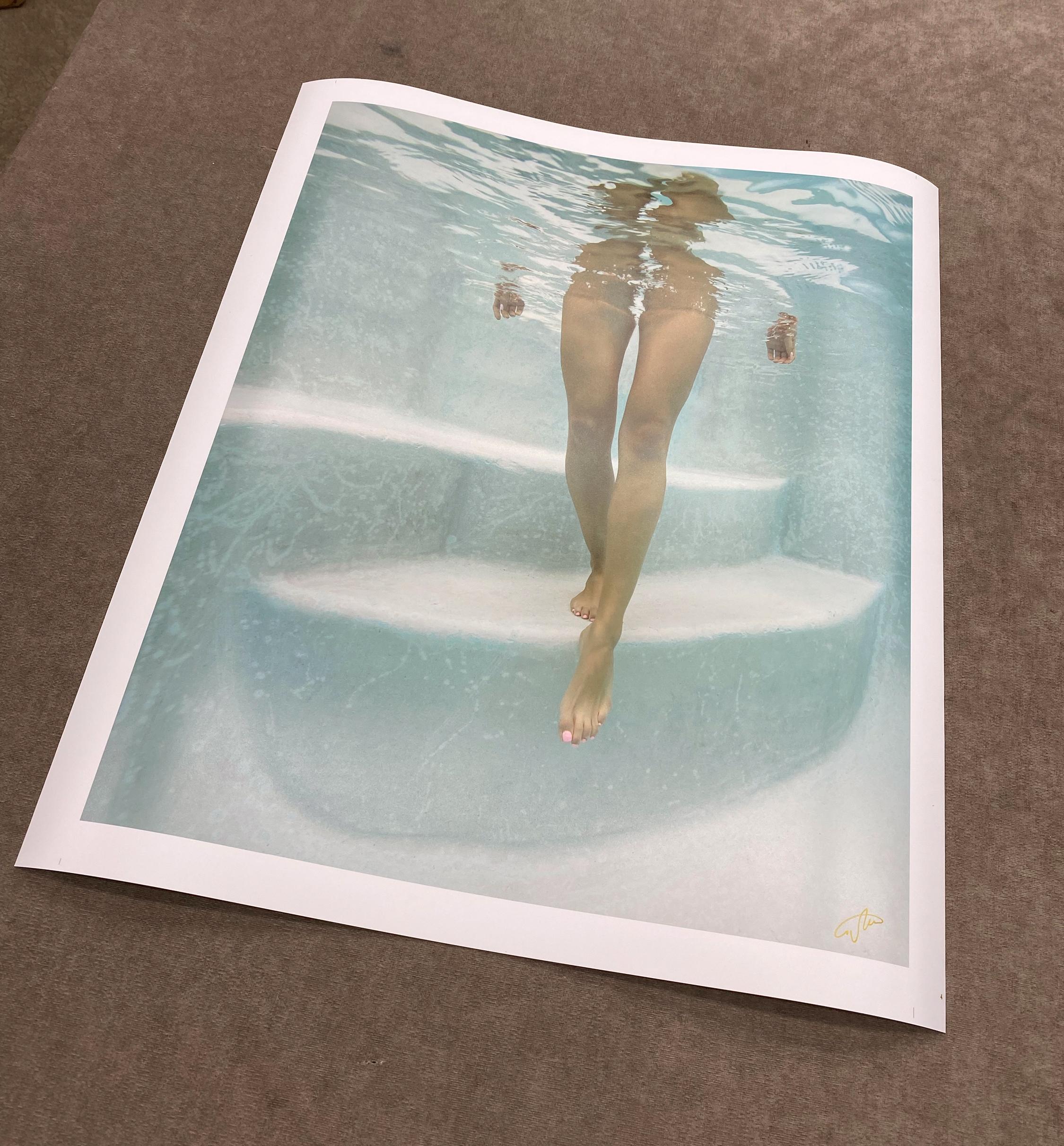 Ein leichtes und sehr ansprechendes Unterwasserfoto eines Mädchens, das die Stufen im Schwimmbecken zu Ihnen hinuntergeht. Das hellblaue Foto zeigt weder einen Badeanzug noch Stellen, an denen man einen Badeanzug erwarten würde. Dieses Foto findet