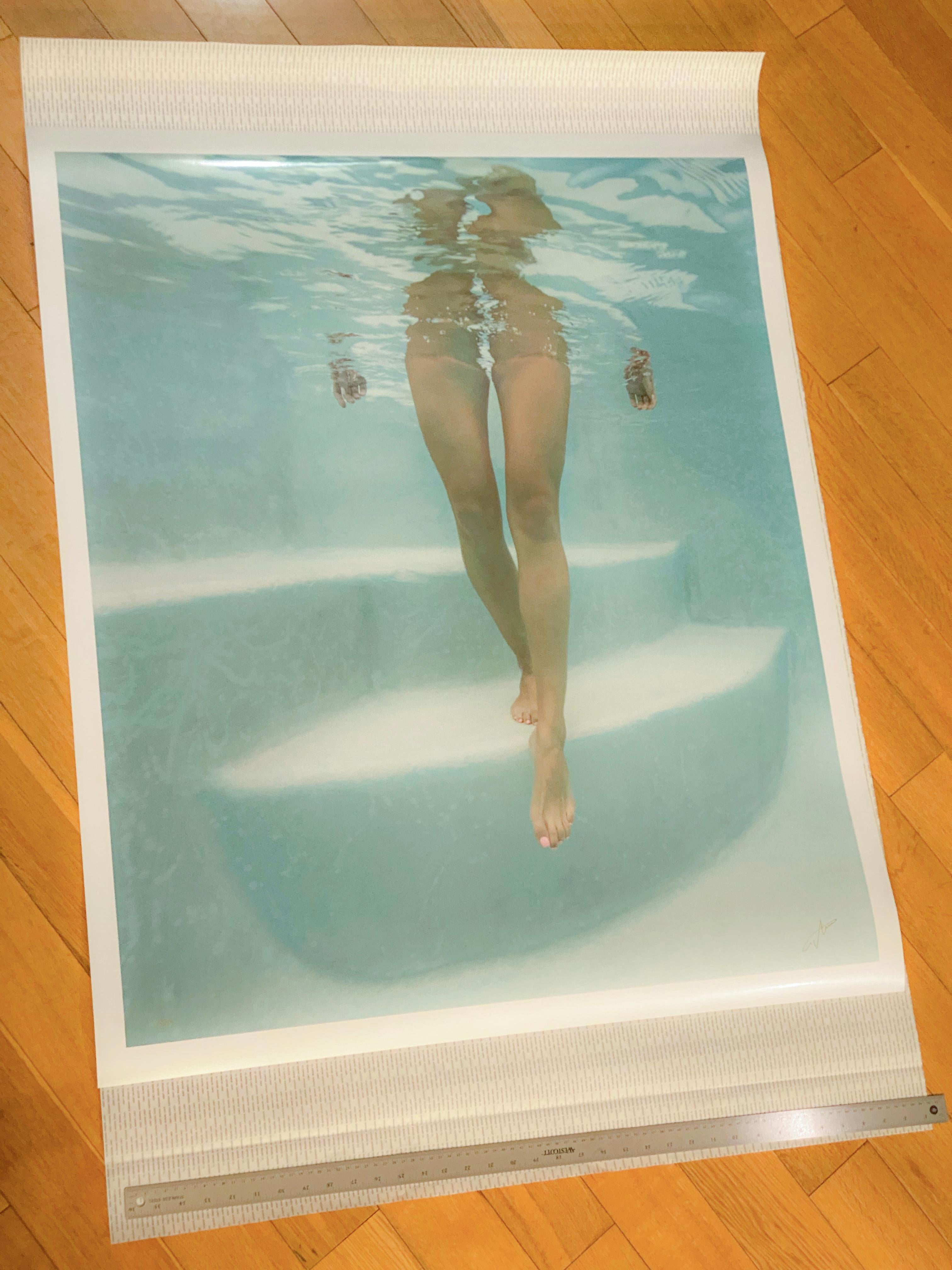 Una fotografía subacuática ligera y muy favorecedora de una chica que baja los escalones de la piscina hacia ti. La fotografía azul claro no muestra ningún bañador ni ningún lugar donde cabría esperar un bañador. Esta fotografía llama mucho la