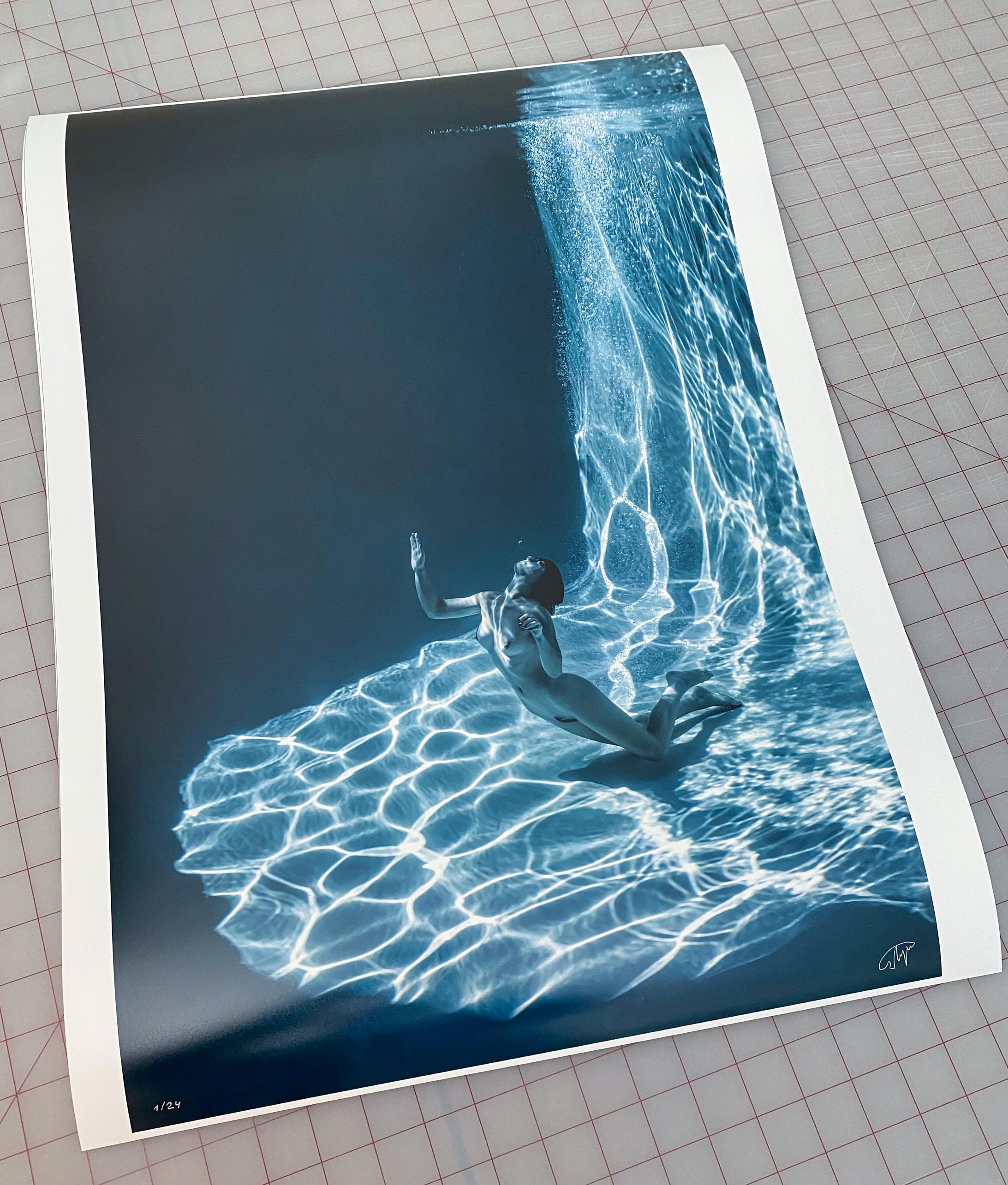 Eine schöne  und mysteriöses Unterwasserfoto einer jungen nackten Frau, die langsam durch das Wasser des Schwimmbeckens an die Oberfläche schwimmt.  Diese monochromatische, aquatisch getönte Fotografie ist Teil der Serie Marble