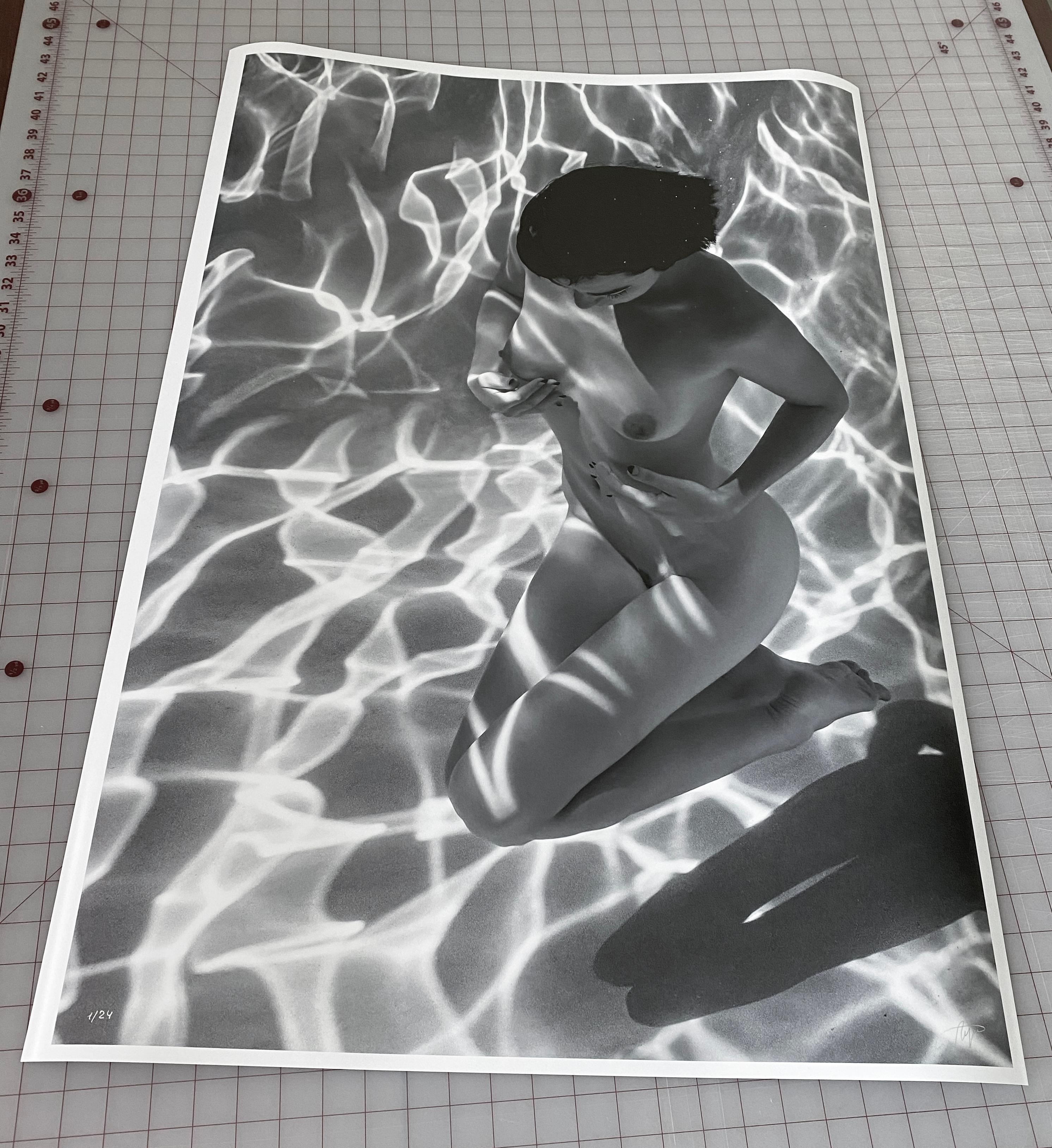 An underwater black and white photograph of a beautiful naked model on her knees at the bottom of the pool.

Original gallery quality archival pigment print on paper signed by the artist.
Limited edition of 24.
The artwork is furnished with
