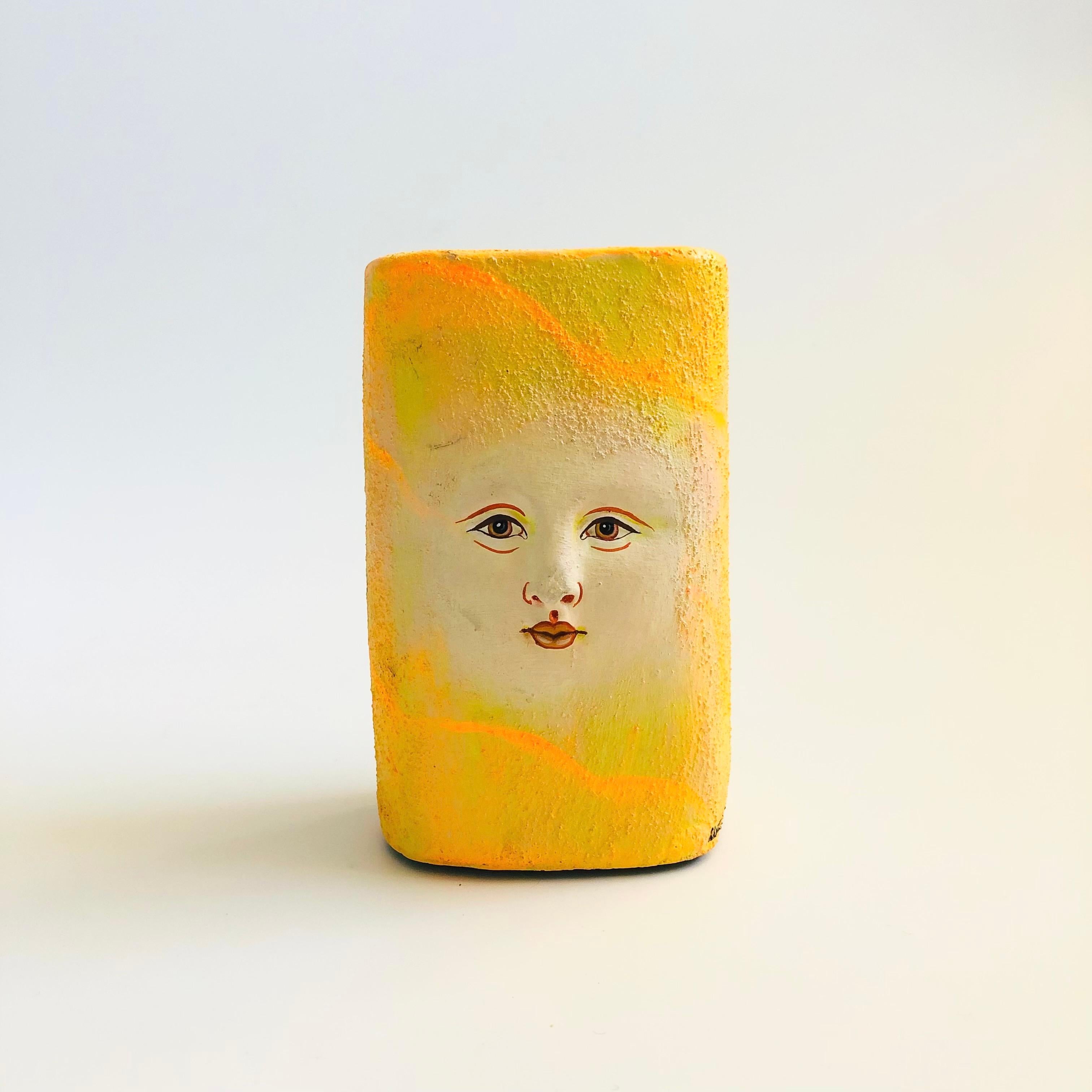 A vintage postmodern pottery sculpture. Made by Mexican cubist artist, Alexander Flores. Curved blocky shape with a face in the center. Textured yellow glaze. Signed on the bottom and with the original sticker on the base.

