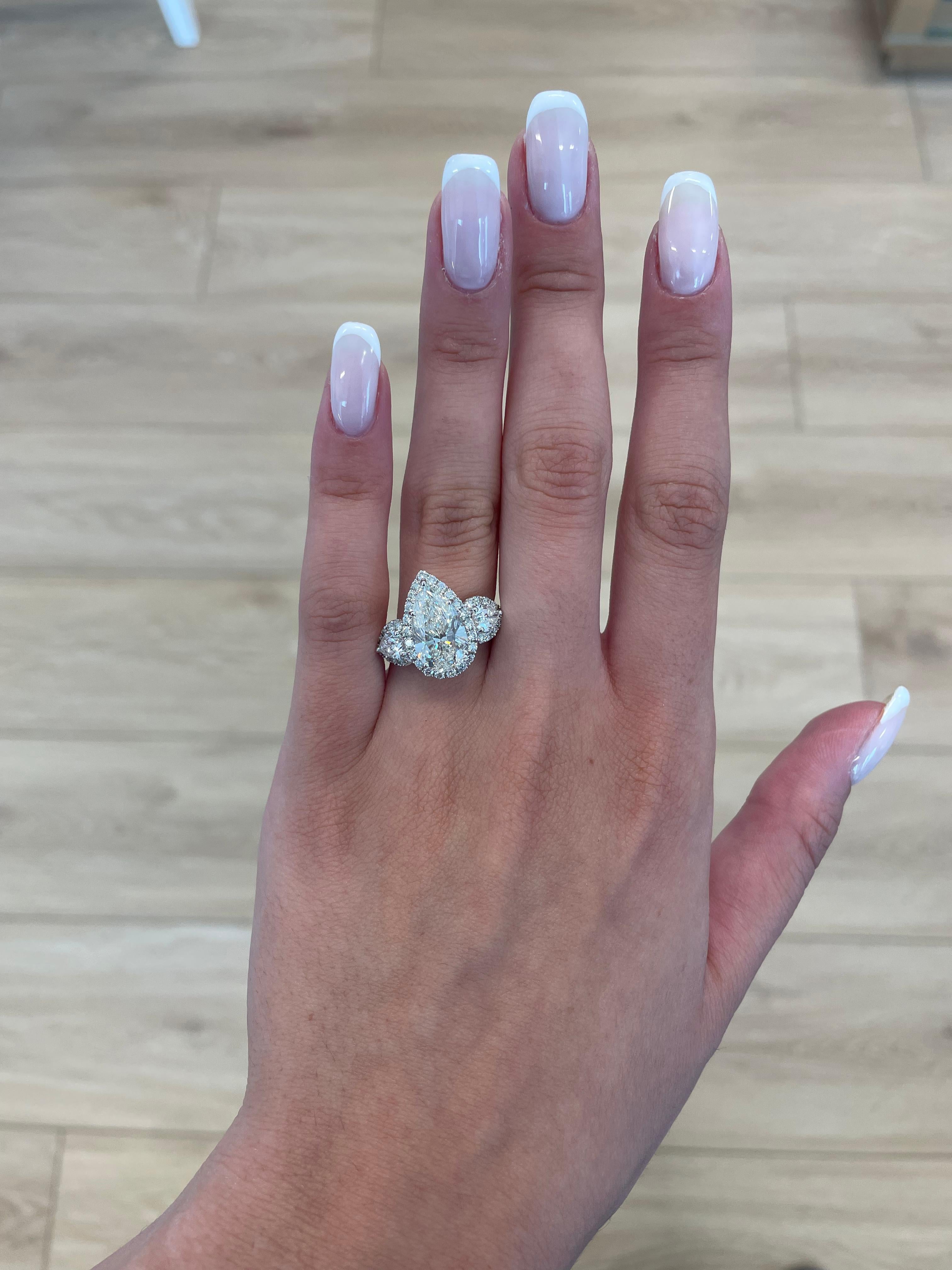 Stunning diamond three-stone engagement ring with halo, GIA certified. High jewelry by Alexander Beverly Hills.
5.85 carats total diamond weight.
4 carat pear shape diamond, GIA certified. J color grade and VS2 clarity. Complimented by 2 pear shape