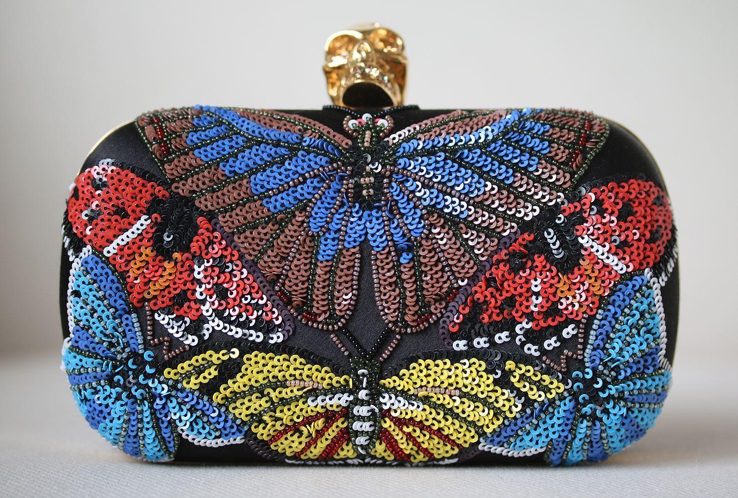 Black and multicolour beaded butterfly embroidery Classic Skull Clutch. Features Swarovski crystal detail skull clasp closure. Satin body of the clutch and a chain strap. Brass hardware with a gold finish. 80% Brass, 20% satin. Does not come with a