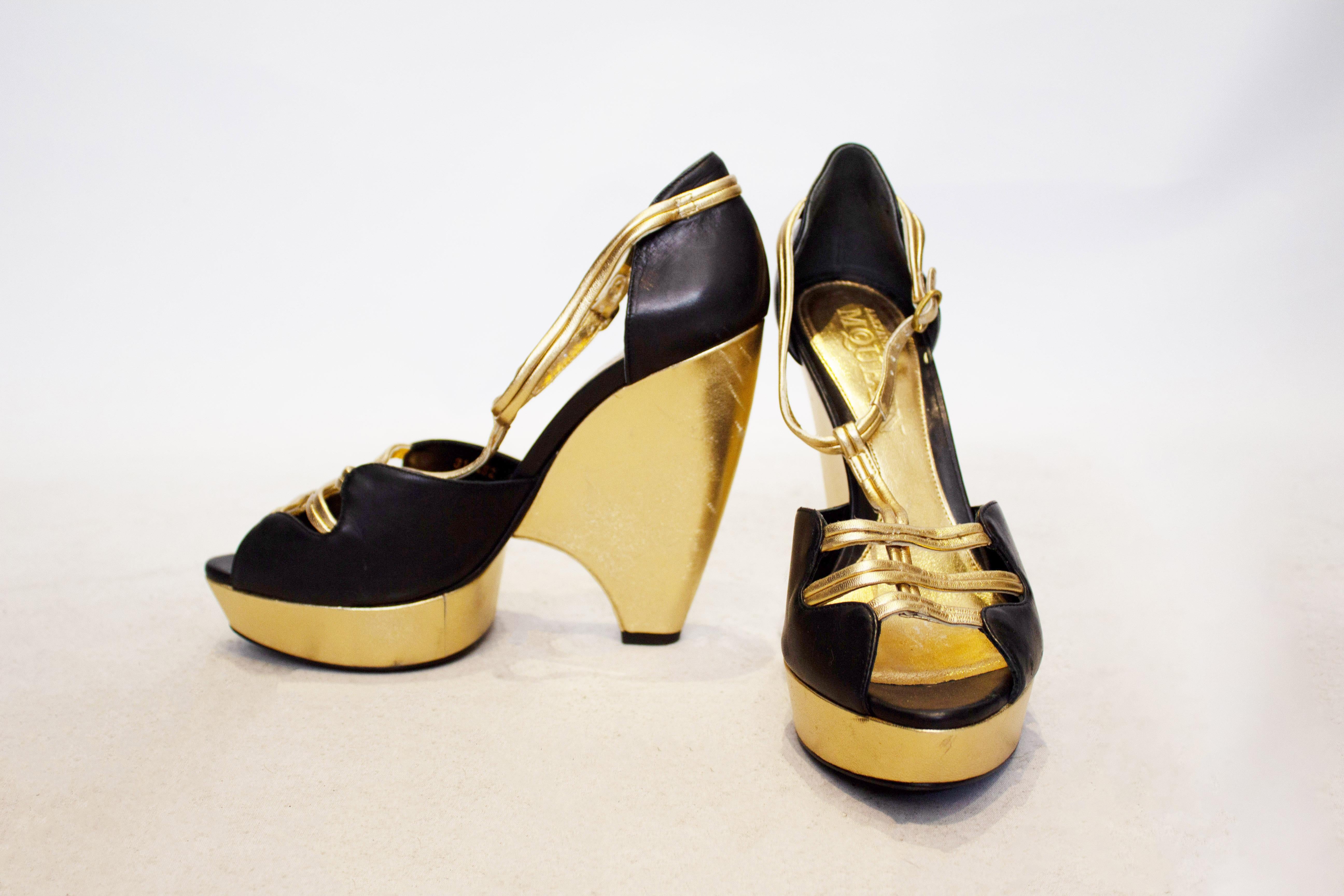 A head turning pair of shoes by Alexander Mcqueen.  The shoes have a gold wedge , with black uppers and gold leather detail. The heel height is 5 1/2 '' and they are marked size 39.