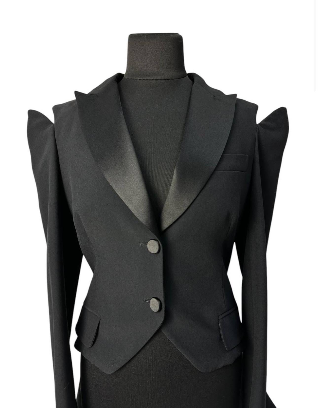

Die skulpturale Schnittführung, die betonten Schultern und der asymmetrische Saum machen diesen Blazer zu einem echten Modestatement. Der tiefschwarze Farbton und die Satinrevers verleihen ihm Eleganz, während die kühne Silhouettenarchitektur