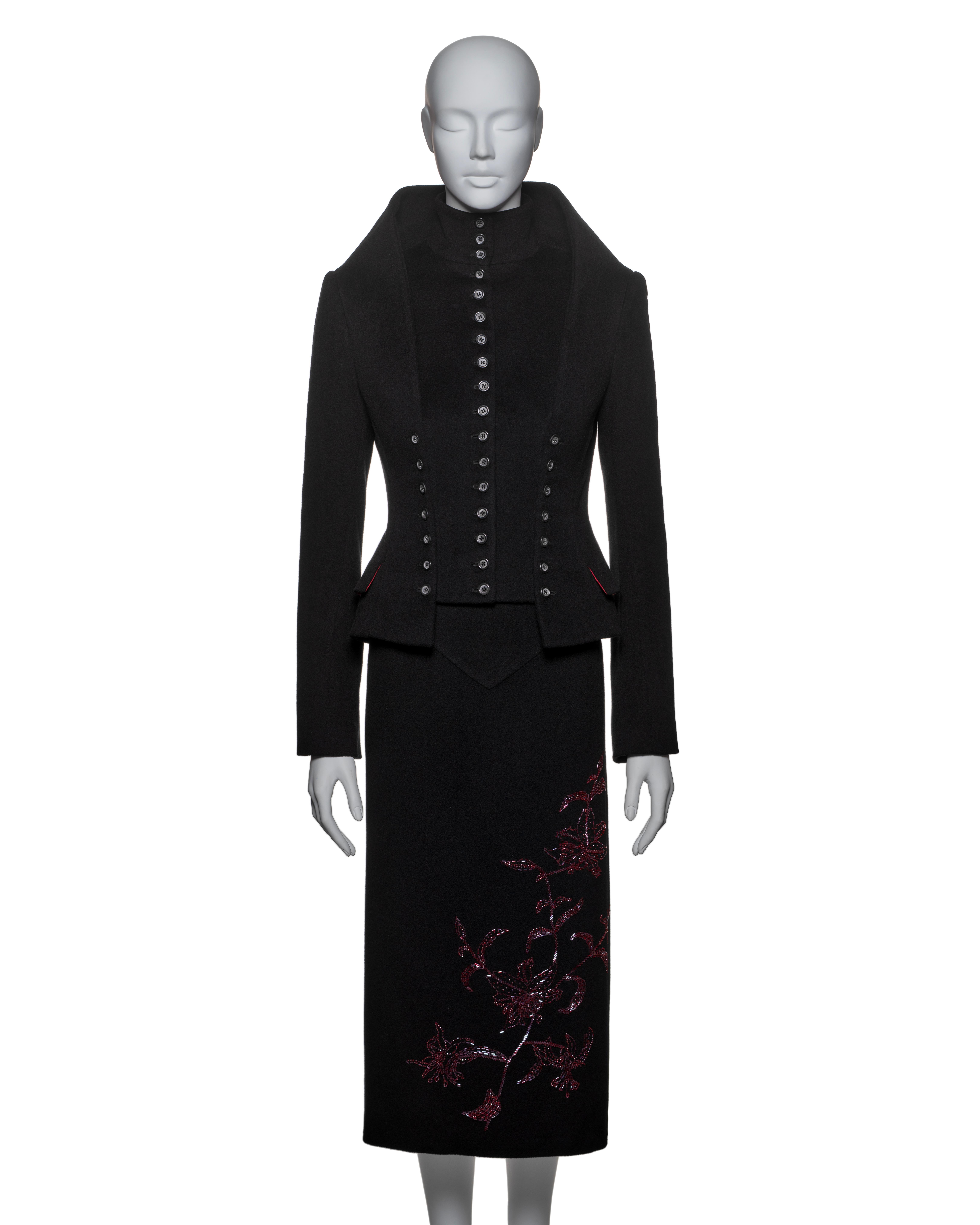 Alexander McQueen suit crafted from black cashmere, featuring a sharply tailored jacket with standing shoulders and a funnel collar. The jacket is adorned with 31 horn buttons and has a precisely fitted waist. Both the jacket and the matching pencil