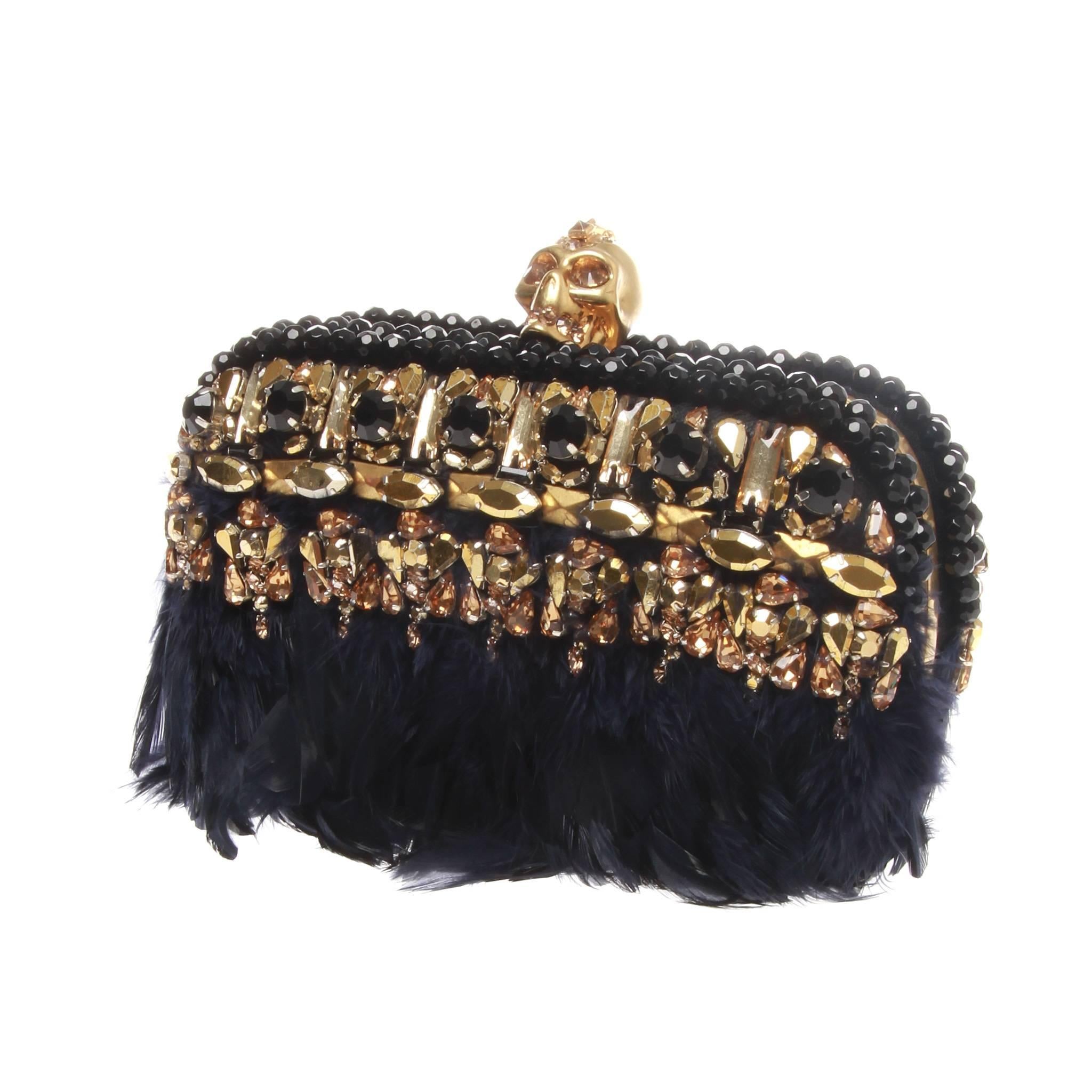 Alexander McQueen skull box clutch featuring goldtone hardware, black and gold beading and navy feathers. Swarovski crystal encrusted skull works as pop clasp at top. Box interior lined with black lambskin. 

Made in Italy 