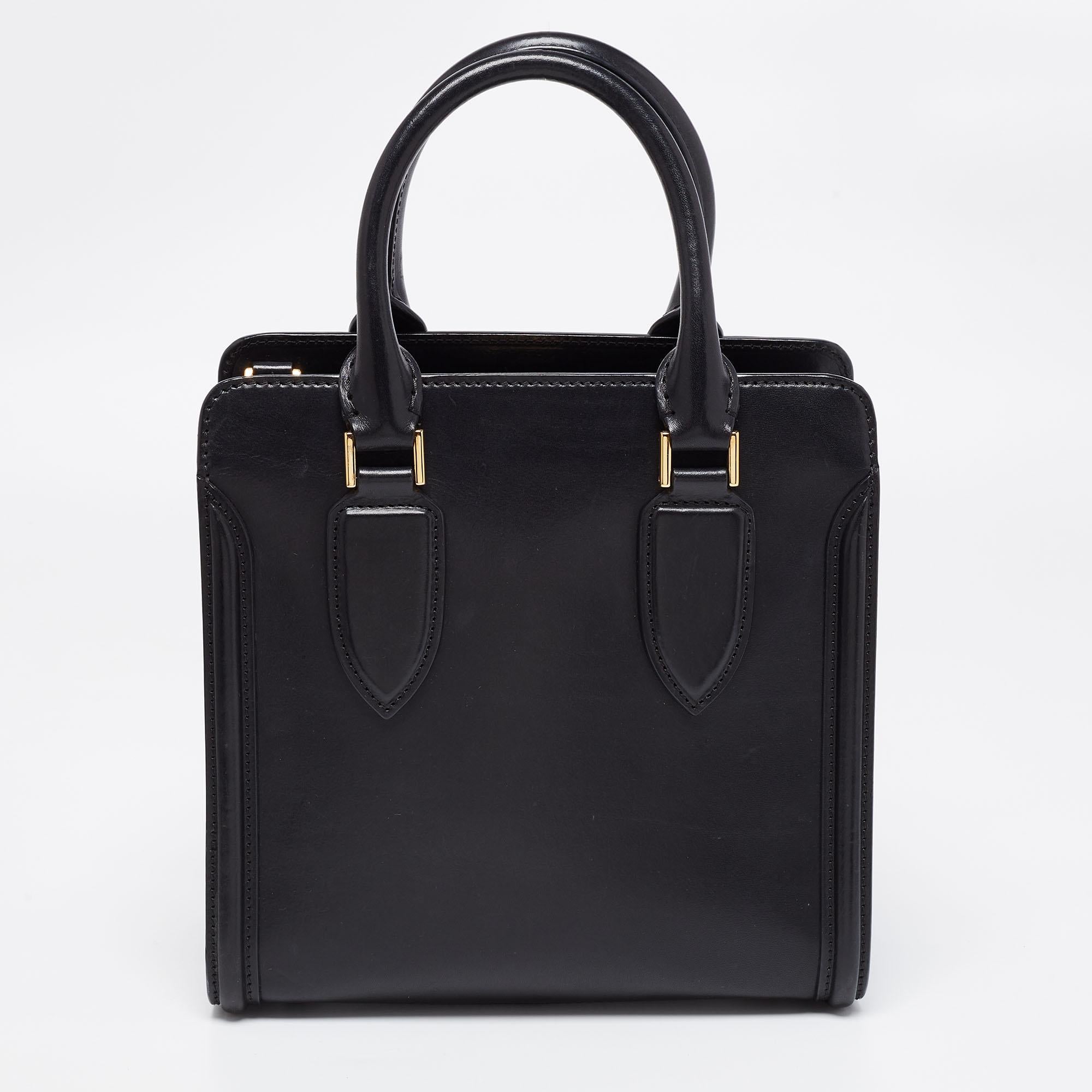 Every woman needs a bag that is pretty and functional, just like this tote bag from Alexander McQueen. Crafted from leather, it has been styled with a flap leading to a spacious fabric interior and it is held by two top handles. This is definitely
