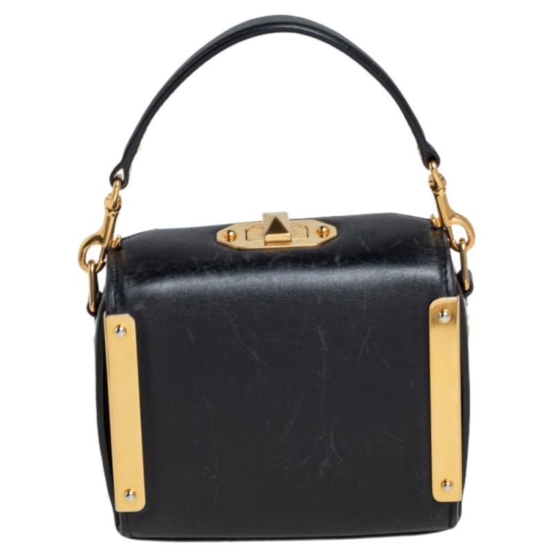 Die feine Kunstfertigkeit und die schlanke Struktur der Tasche spiegeln die jahrelange Handwerkskunst von Alexander McQueen wider. Die aus Leder gefertigte Tasche in Kastenform verfügt über einen Griff an der Oberseite und goldfarbene Metallstangen