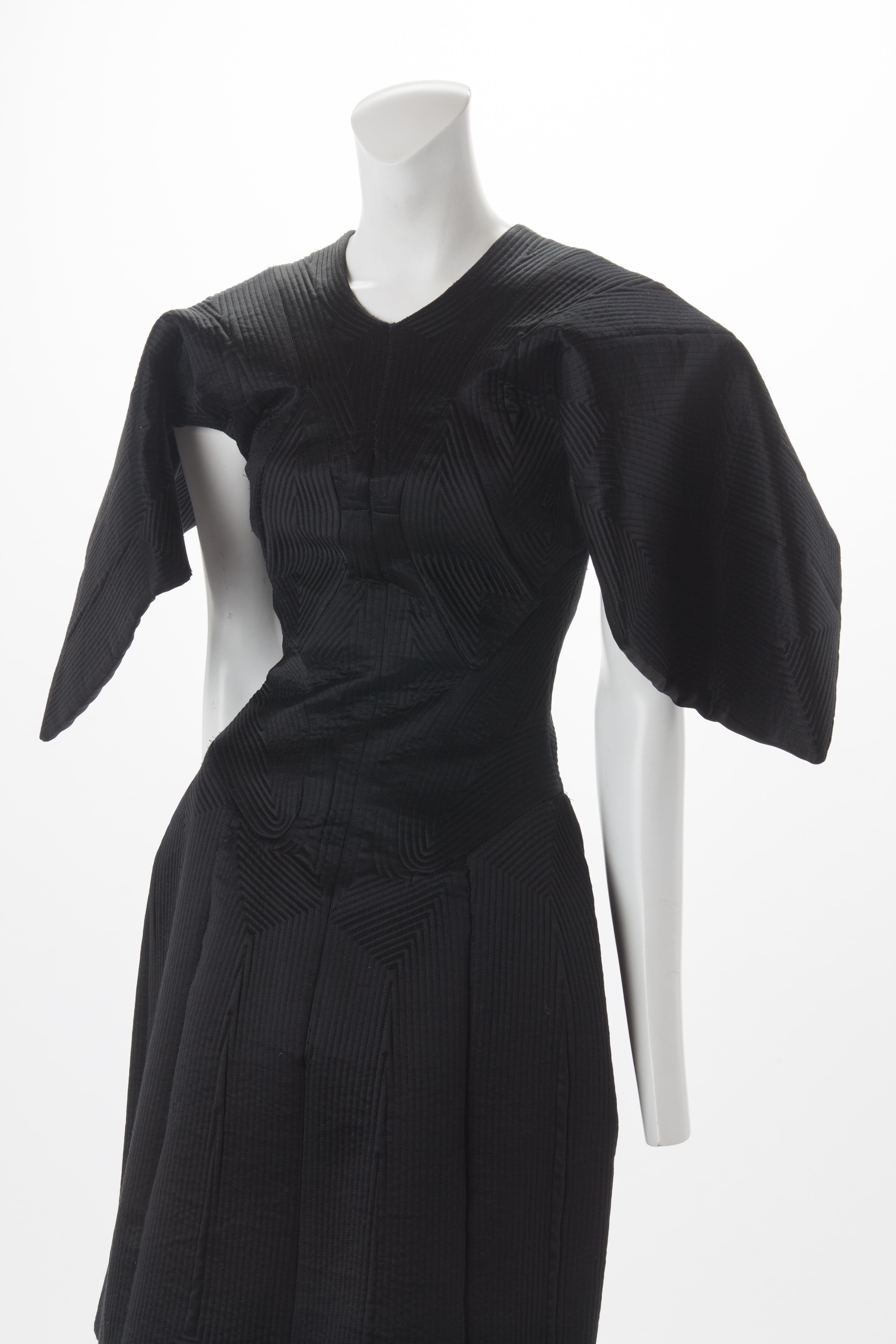 Alexander McQueen Black Quilted Satin Cocktail Dress with Batwing Sleeves, 2009.
Quilted structured dress with seaming creating geometric pattern throughout. Batwing mid-length sleeves that create a cape-like look from the back of this dress. Hidden