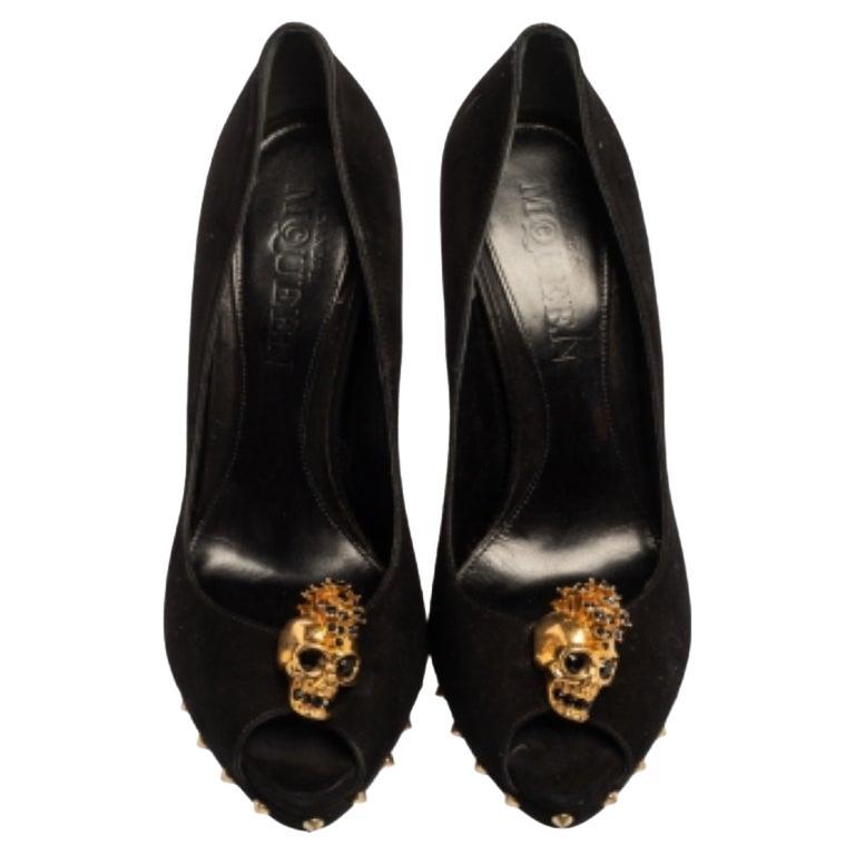 A gorgeous pair, these black-hued Alexander McQueen pumps combine femininity with boldness. These suede peep-toe pumps feature gold-tone skull embellishments at the vamps and stud lined platforms. They come with 15 cm tall covered heels.