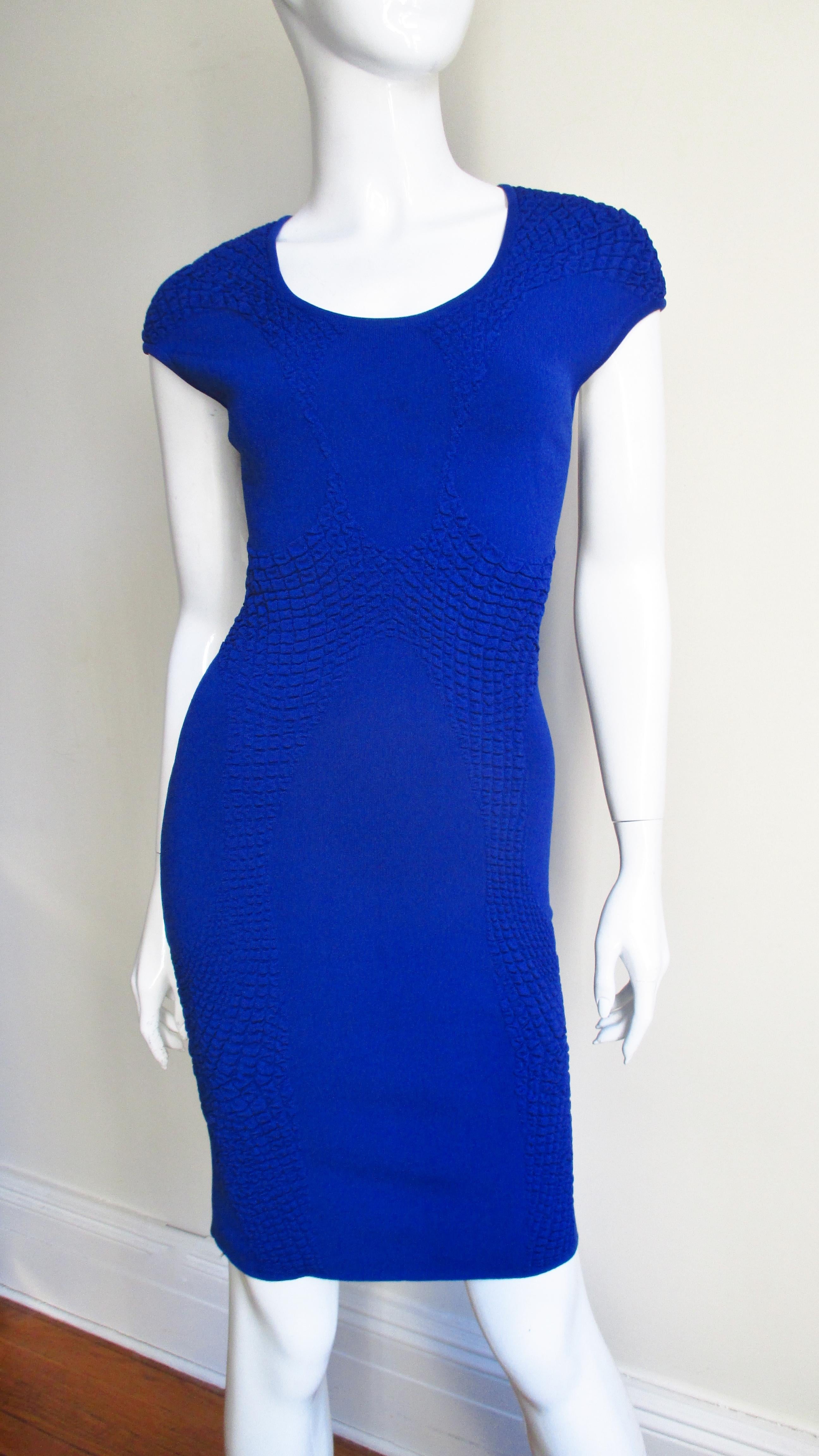 A vibrant blue knit bodycon dress from Alexander McQueen. It is highlighted down the front and back with strategically placed figure enhancing subtle pebble textured knit detail in the same fabric. It has a crew neckline and cap sleeves. There are