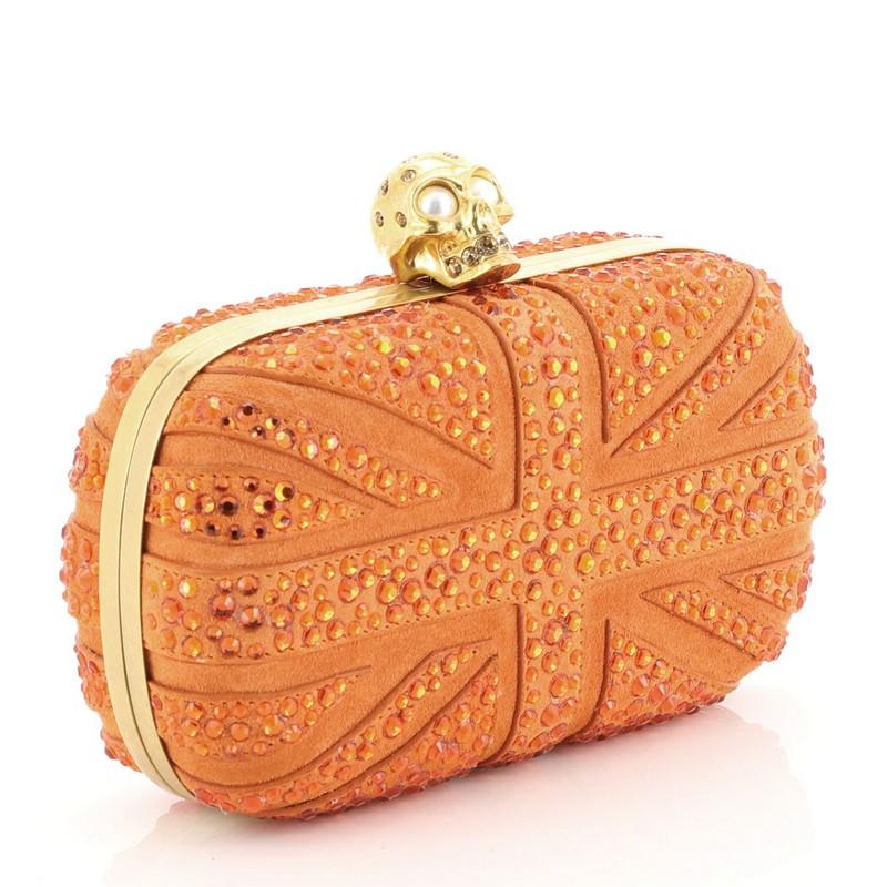 This Alexander McQueen Britannia Skull Box Clutch Studded Suede Small, crafted with orange studded suede, features Union Jack flag inspired crystal studs design, hinged metal frame, and gold-tone hardware. Its skull clasp closure opens to an orange