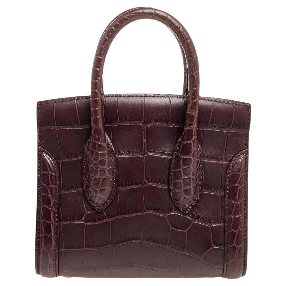 Every woman needs a bag that is pretty and functional, just like this shoulder bag from Alexander McQueen. Crafted from croc-embossed leather, it is styled with an alcantara interior and held by two top handles. This is definitely one handy bag that
