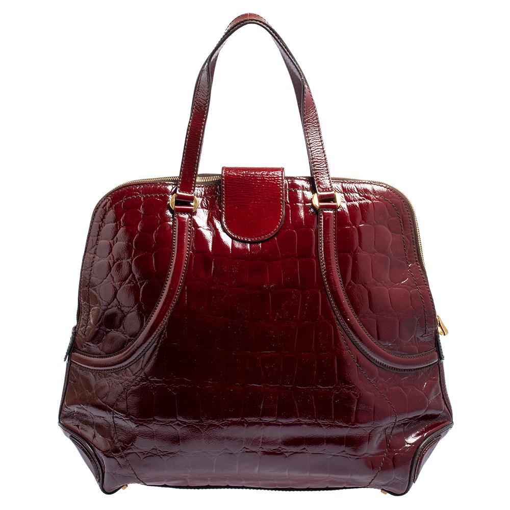Stylish, striking and perfect to carry all your essentials, this bag by Alexander McQueen is a pick that will never disappoint. It has been crafted from croc-embossed patent leather and comes in a lovely shade of burgundy. It is styled with dual