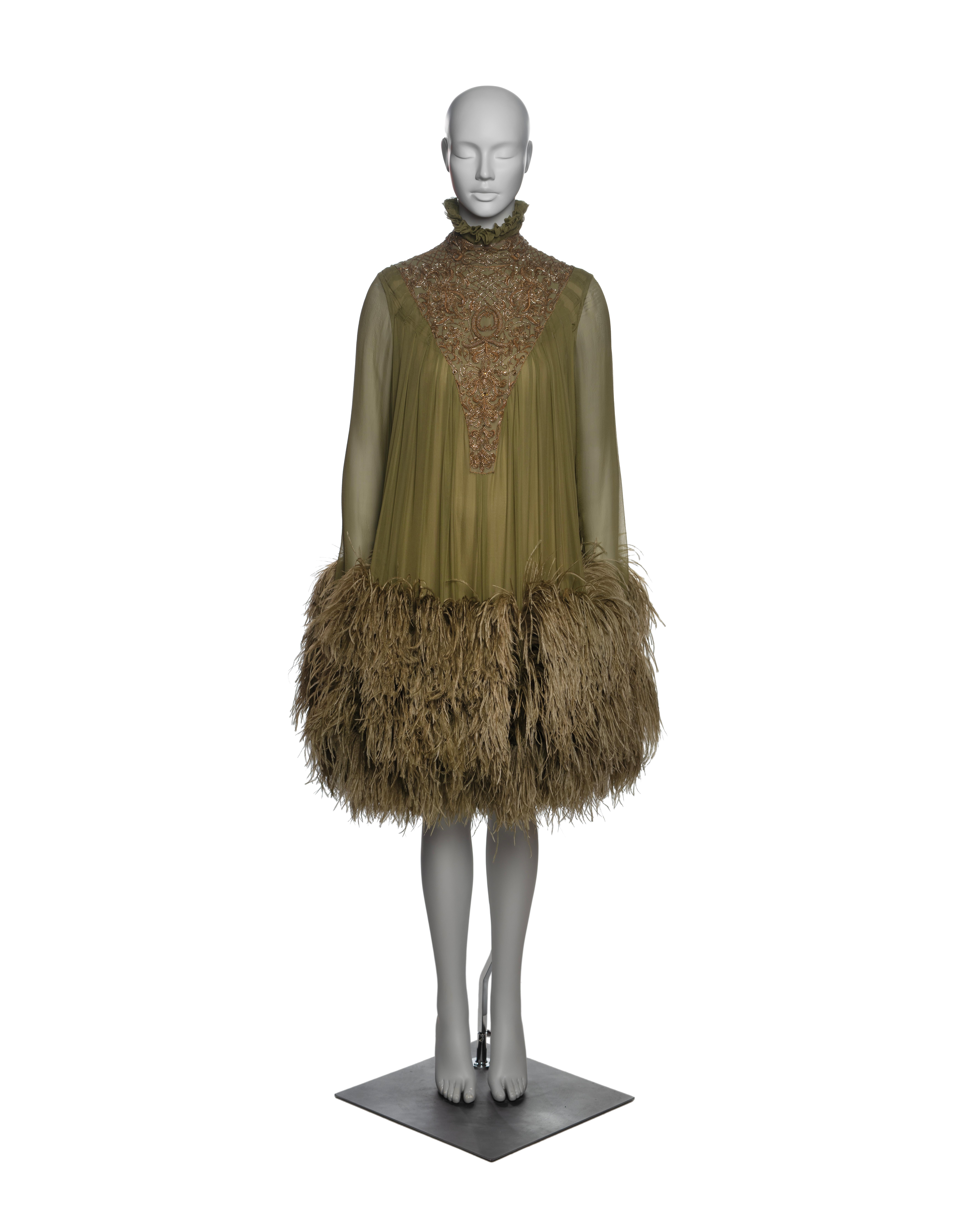 Vestido de noche tipo museo de Alexander McQueen con cuello alto de volantes y elaborados bordados de cuentas de corneta en la parte delantera y trasera. El vestido está confeccionado con capas de gasa de seda plisada verde oliva, mangas largas