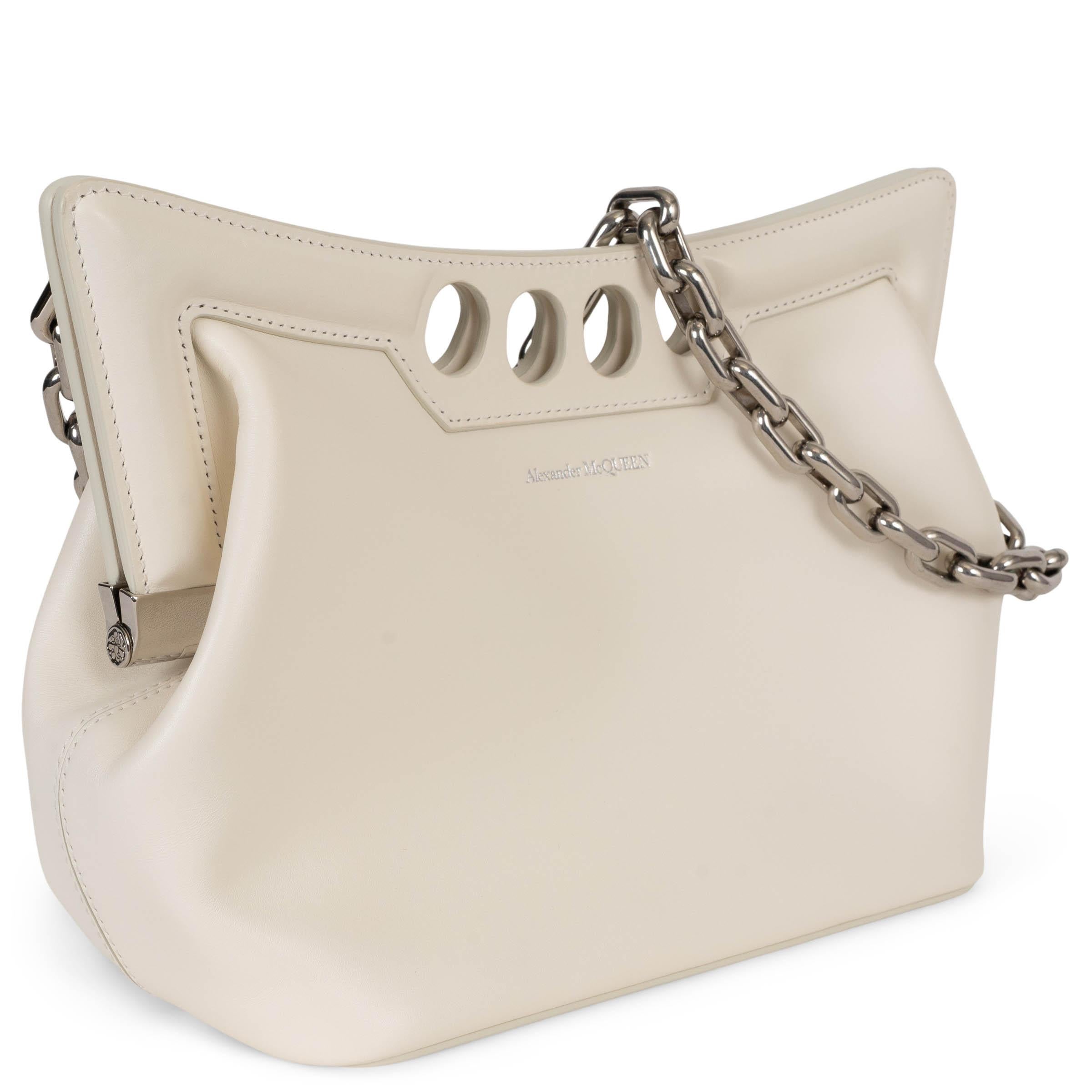 This 100% authentic Alexander McQueen The Peak Small bag in Soft Ivory leather embodies the brand’s signature sculptural elegance. Featuring a supple body contrasted with a structured curved frame top, it is designed with four circular cut-outs for
