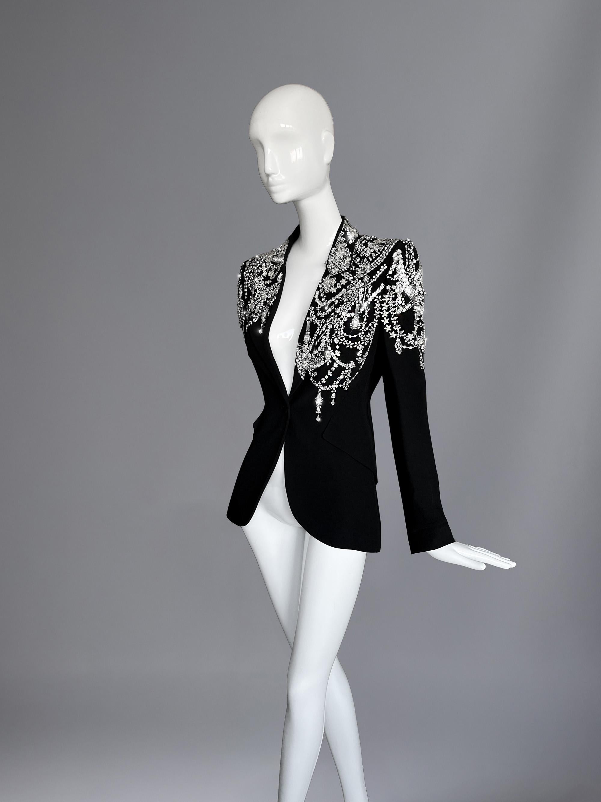 Spectacular Alexander McQueen crystal jacket: armor, sculpture, and seduction. This particular piece is a masterclass in opulence and precision: a sharply tailored black blazer whose clean, architectural lines become the canvas for an explosion of
