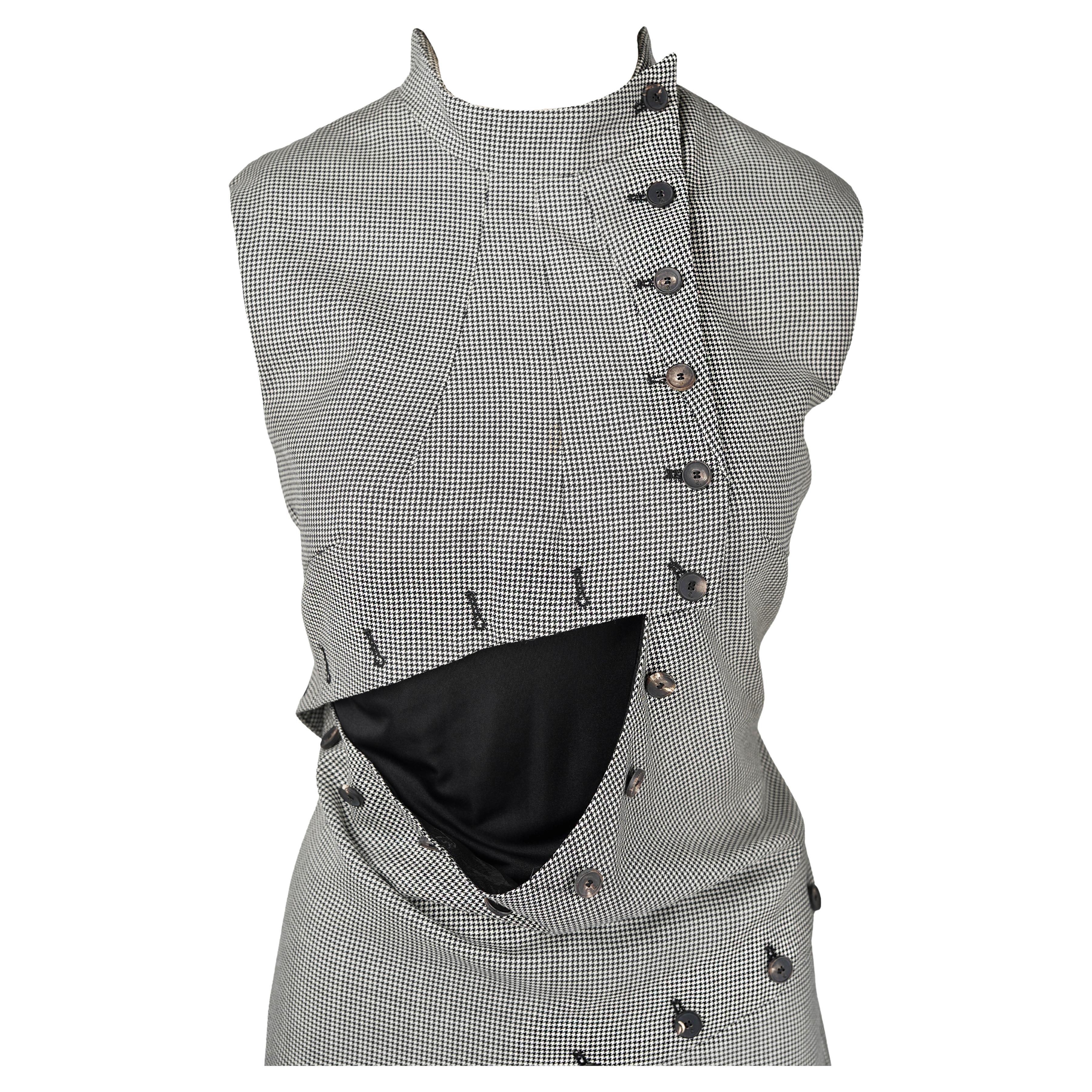 A rare and sculptural piece from Alexander McQueen’s Pre-Fall 2013 collection, this dress showcases the house’s mastery of sharp tailoring and architectural deconstruction. Crafted in a refined micro-houndstooth wool, the design features a dramatic