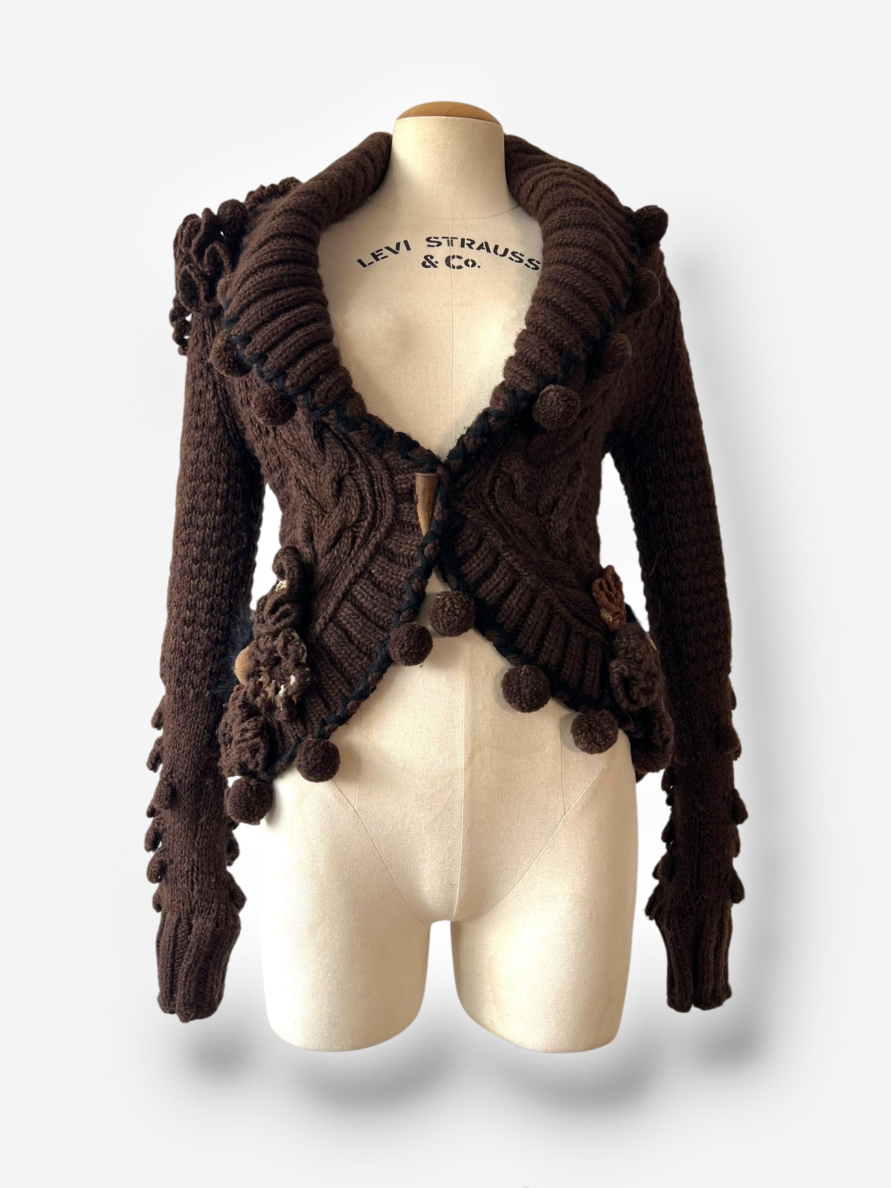 
Único y escultural, este cárdigan de la colección Otoño/Invierno 2005 de McQueen presenta una rica textura de punto, rematada con caprichosos pompones y detalles de volantes. Confeccionada con una lujosa mezcla de alpaca y lana, es perfecta para
