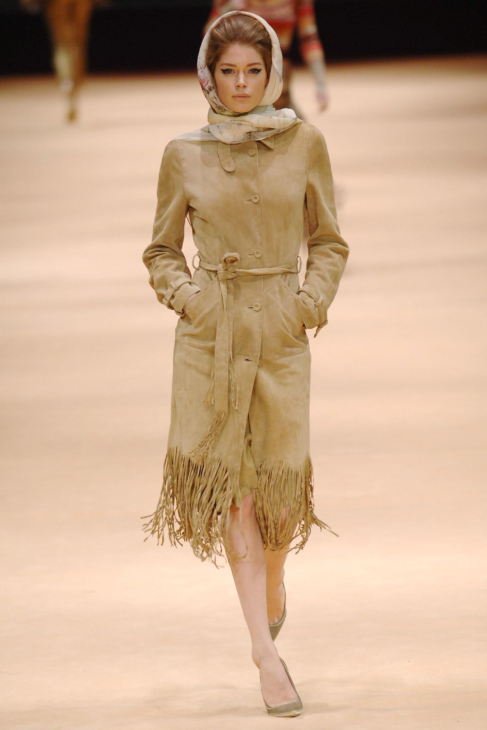 - Diseñado por Alexander McQueen
- Otoño Invierno 2005
- Pieza de pasarela
- Abrigo de ante marrón
- Detalles de flecos en la parte inferior
- Cierre con botones
- Cinturón en la cintura
- Aplicación del cinturón en las muñecas
- Doble capa en la