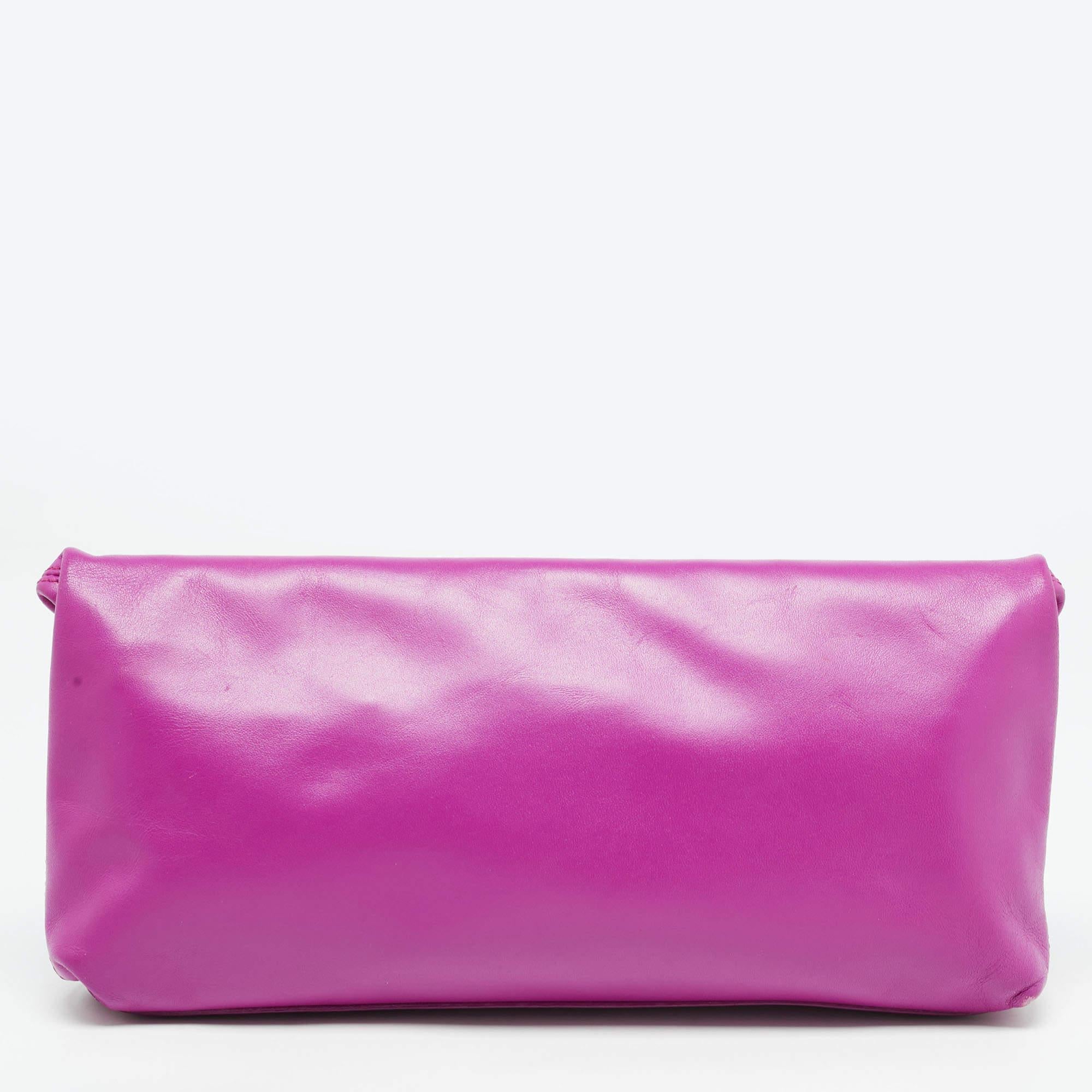 This stunning Alexander McQueen fold over clutch is a perfect party wear accessory with its classic look and a subtle rocker chic style. Crafted in fucshia leather, this clutch features a gold tone studded front along with a skull designed padlock