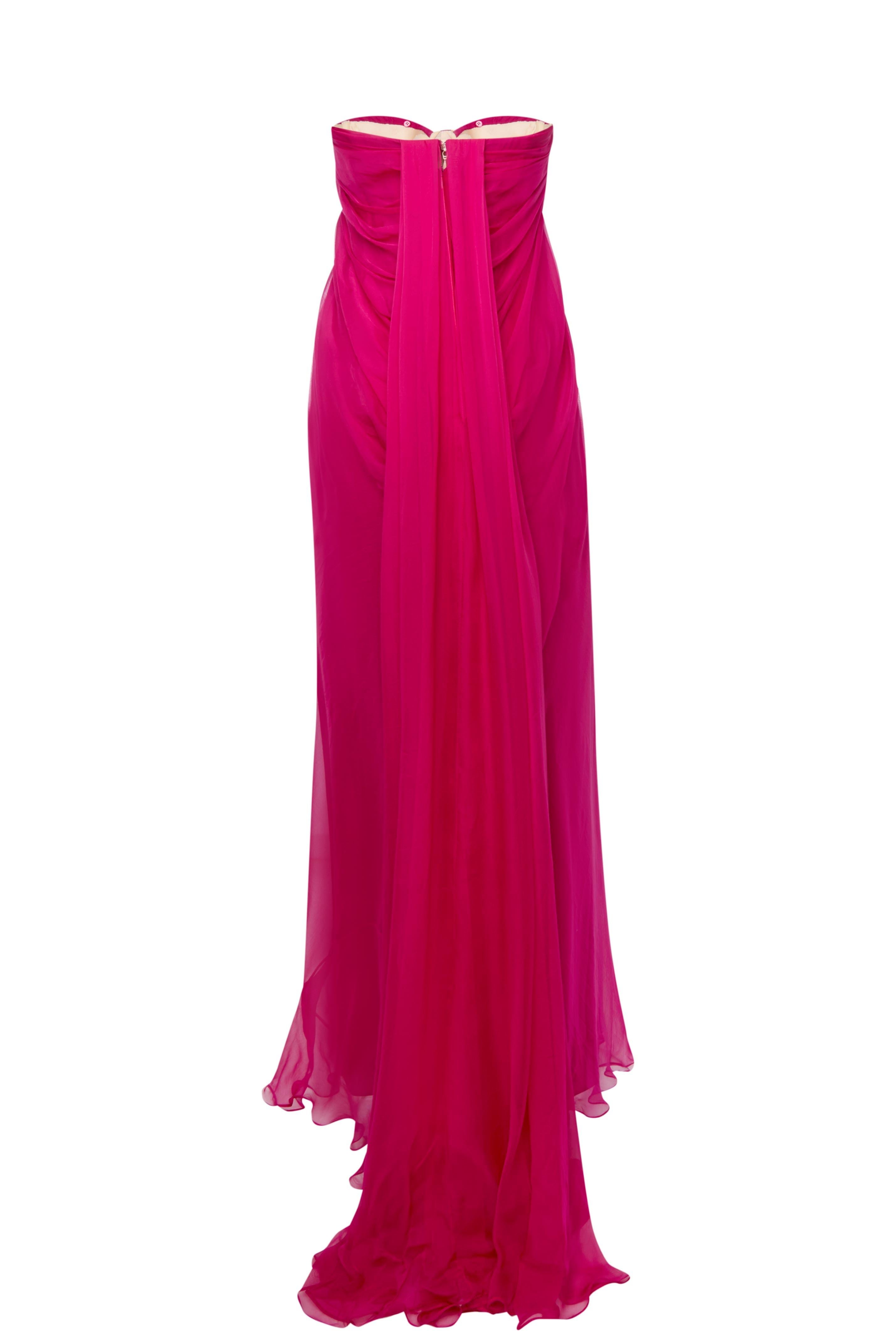 This stunning Alexander McQueen fuchsia silk dress is a true statement piece from the early 2000s, embodying the brand’s signature avant-garde elegance. Designed to create a striking silhouette, this strapless dress features soft pleats and a