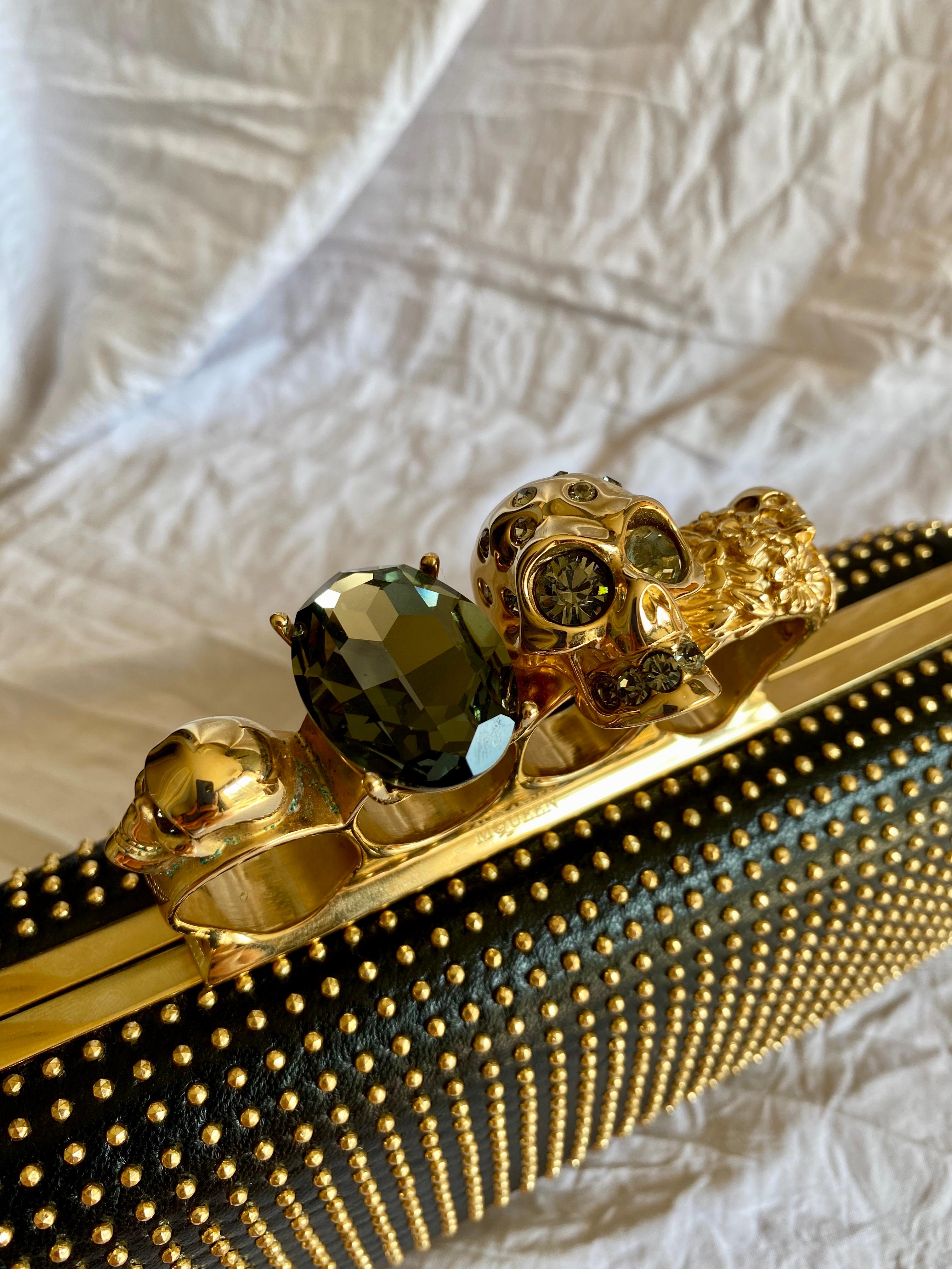 McQueen spielt bei dieser Clutch wunderbar mit Textur und Funktion. Sie ist mit einem Vier-Ring-Verschluss ausgestattet und besteht aus vollnarbigem Leder:: goldfarbener Hardware und Swarovski-Kristalldetails. 

Zustand: Wie neu:: nie benutzt 
