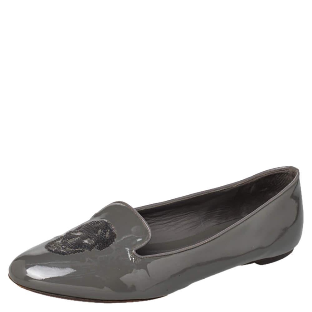 Ces pantoufles de smoking très appréciées d'Alexander McQueen sont à la fois confortables et élégantes ! Confectionnées en cuir verni d'un gris envoûtant, ces pantoufles sont ornées de motifs de têtes de mort sur le dessus. Elles sont dotées d'un