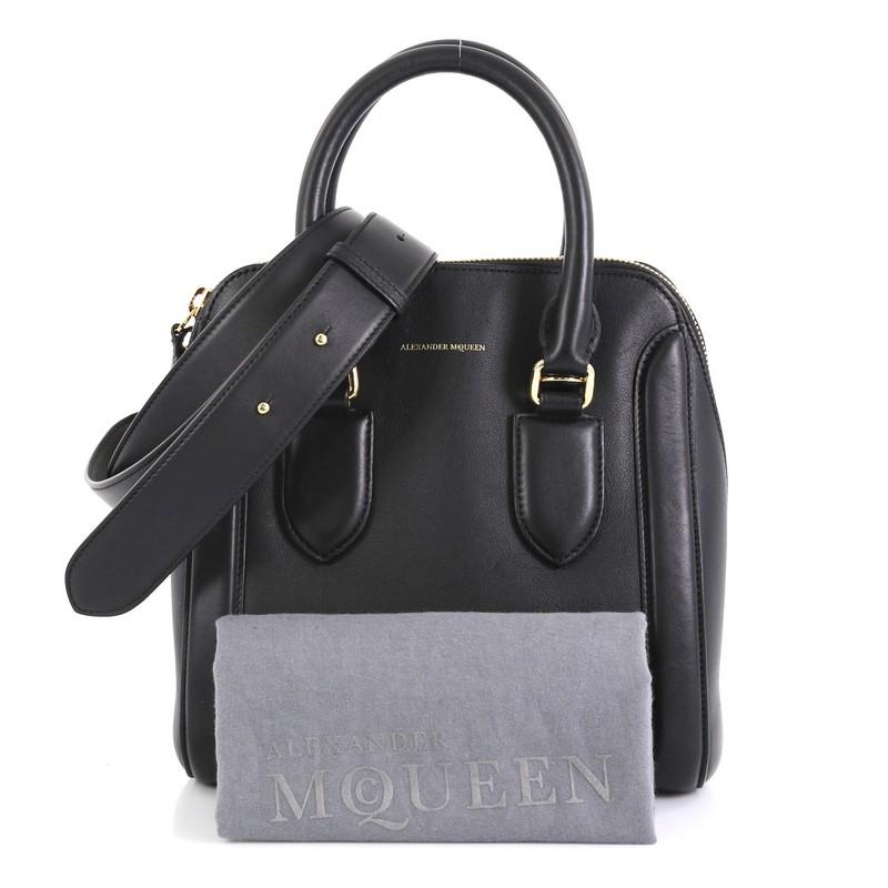 This Alexander McQueen Heroine Convertible Bowling Bag Leather Medium, crafted in black leather, features dual rolled leather handles, oversized side zipper details, embossed logo at the center, and gold-tone hardware. Its flap closure opens to a