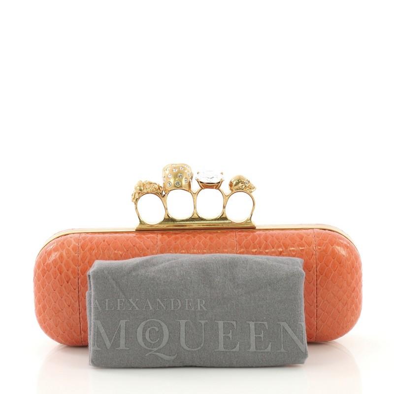 This Alexander McQueen Knuckle Box Clutch Python Long, crafted from genuine orange python, features a knuckle handle embellished with crystals, bejeweled skull and gold-tone hardware. It opens to a coral leather interior. **Note: This item can only