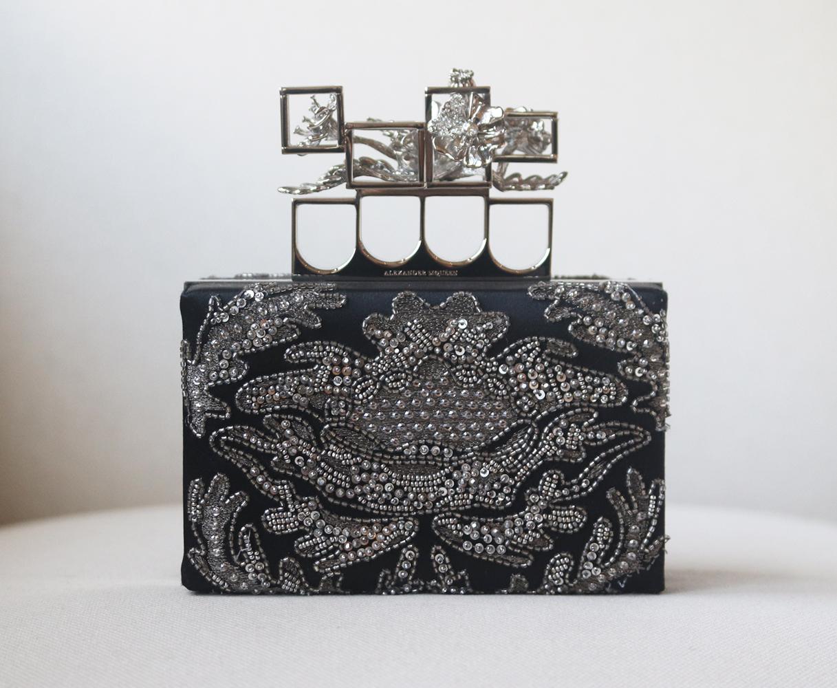 Made in Italy, Alexander McQueen's black satin box clutch is lavishly embellished with gunmetal embroidery, sequins, beads and Swarovski crystals, the polished silver-tone brass knuckle clasp is strikingly detailed with caged poppies.
Black satin