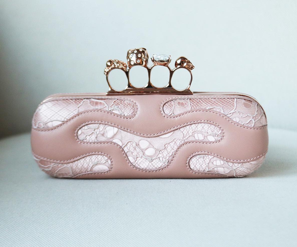 Fashion-forward women will adore Alexander McQueen's knuckle clutch updated in pink lace-covered satin and leather, it has been adorned with pink Swarovski crystal embellishment set on a rose-gold frame. 
Pink lace and leather, gold