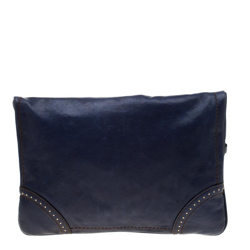 This stunning Alexander McQueen flappy clutch is a perfect party wear accessory with its classic look and a subtle rocker chic style. Crafted in navy blue leather, this clutch features a cute British Royal Guard charm along with a decorated
