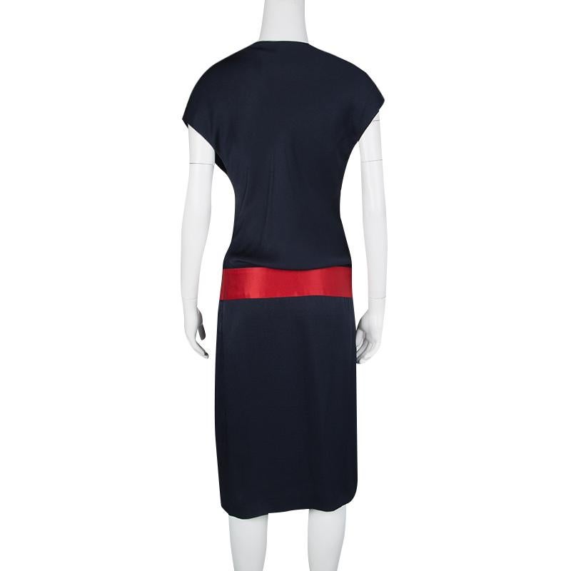 This is a dress that simply screams glamour and festivity in all of its design. The fitted body is crafted out of pure silk in a gorgeous navy blue and is accented by a bold red belt detailing at the drop waist. The knot detail at the neck adds to