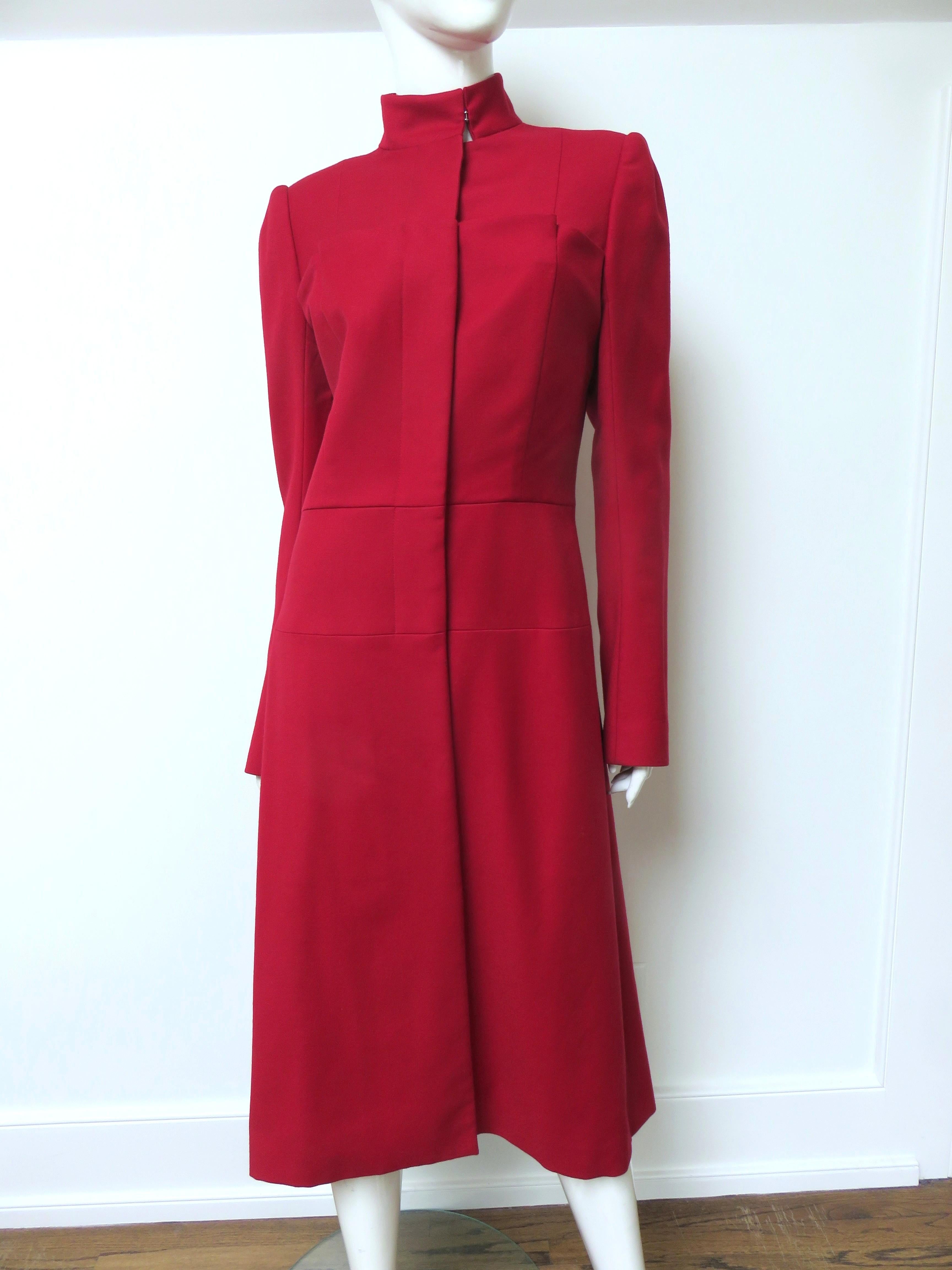 Un fabuleux manteau en laine rouge signé Alexander McQueen. Il présente un col mandarin montant, un devant boutonné avec des boutons assortis dissimulés dans une patte de boutonnage et des pad aux épaules.  Le corsage avant comporte un panneau de