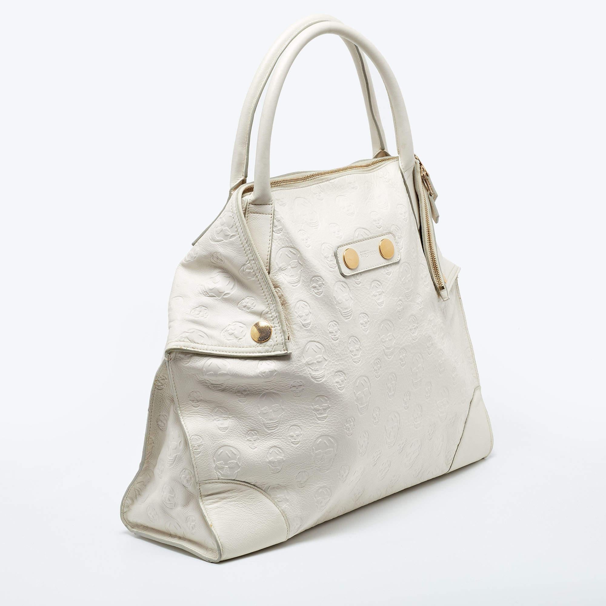 Add a shimmery touch to your outfit with this uniquely shaped yet elegant De Manta tote by Alexander McQueen. The exterior is made from off-white leather, accented with gold-tone metal studs on the front. It features fold up ends and a zipped
