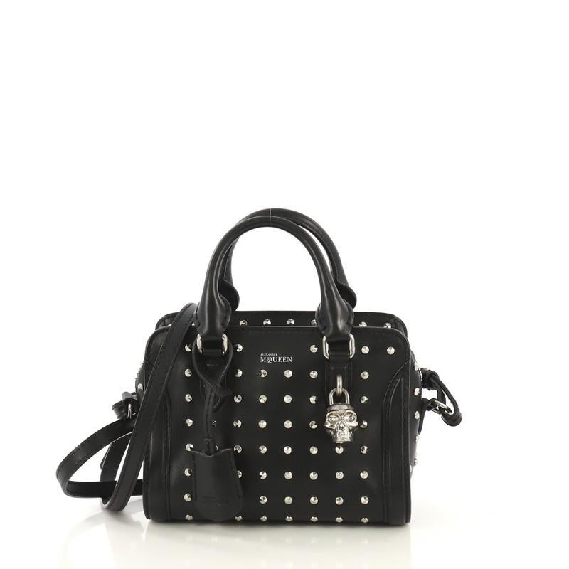 This Alexander McQueen Padlock Zip Around Tote Studded Leather Mini, crafted in black leather, features dual rolled handles, studded spiked detailing, signature skull padlock, and silver-tone hardware. Its zip closure opens to a black fabric