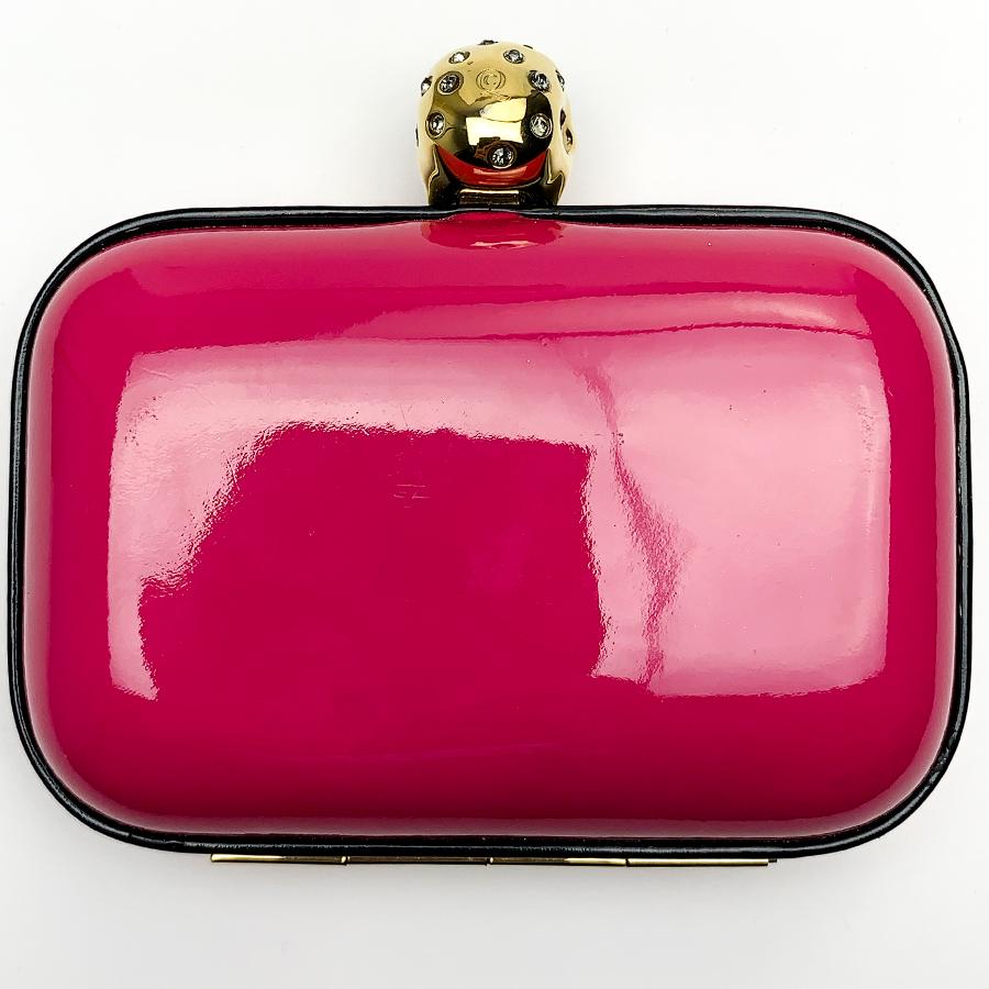 This minaudière is signed by Maison Alexander McQueen. It is a bright pink and it is surmounted on the clasp of a vanity, an allegorical representation of death.
The minaudière is in very good condition. Presence of the brand on the interior velvet,