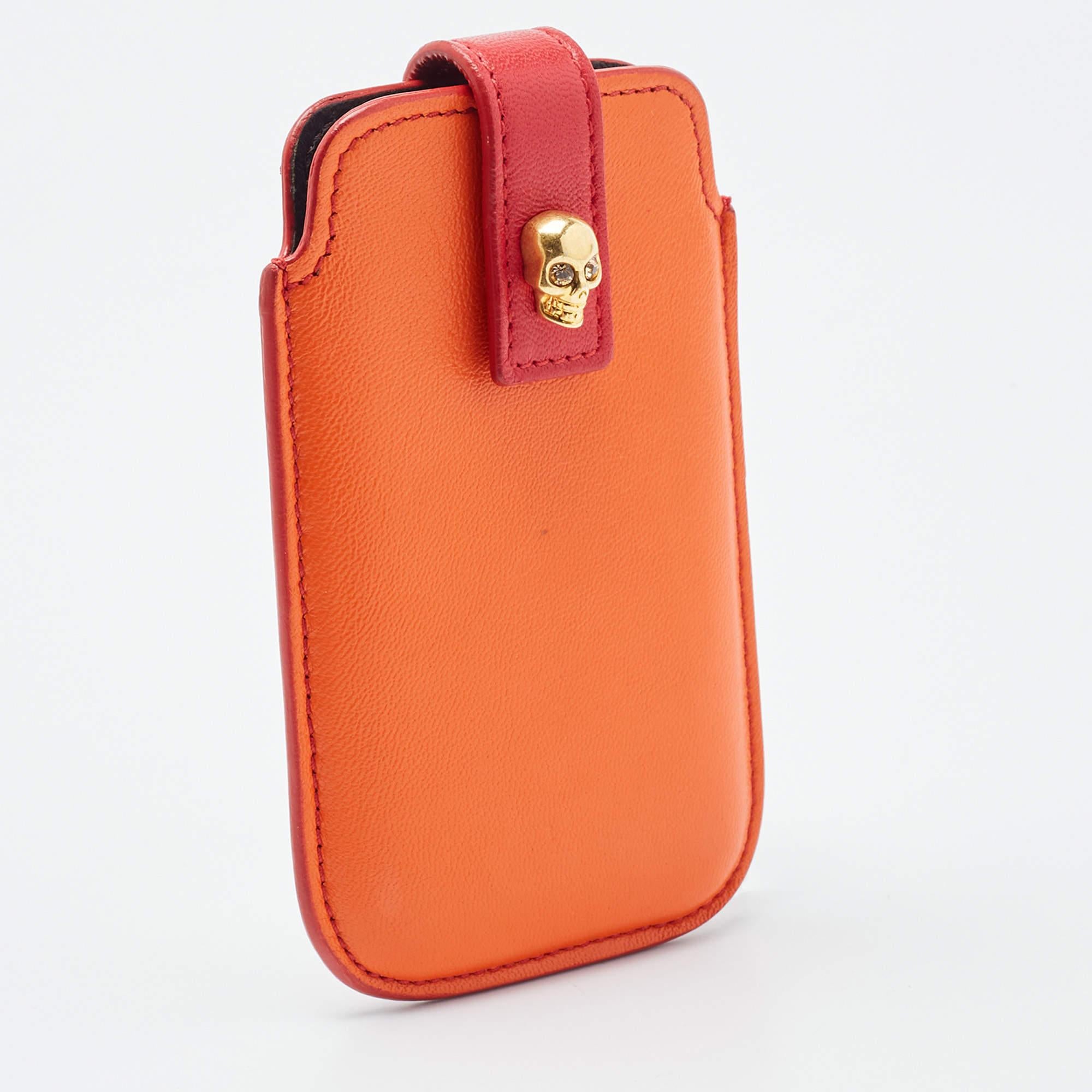 Protect your phone with a pop of color with this Alexander McQueen phone case. Its orange leather exterior is coupled with red backing and a flap with a snap closure and a skull embellishment on the front.