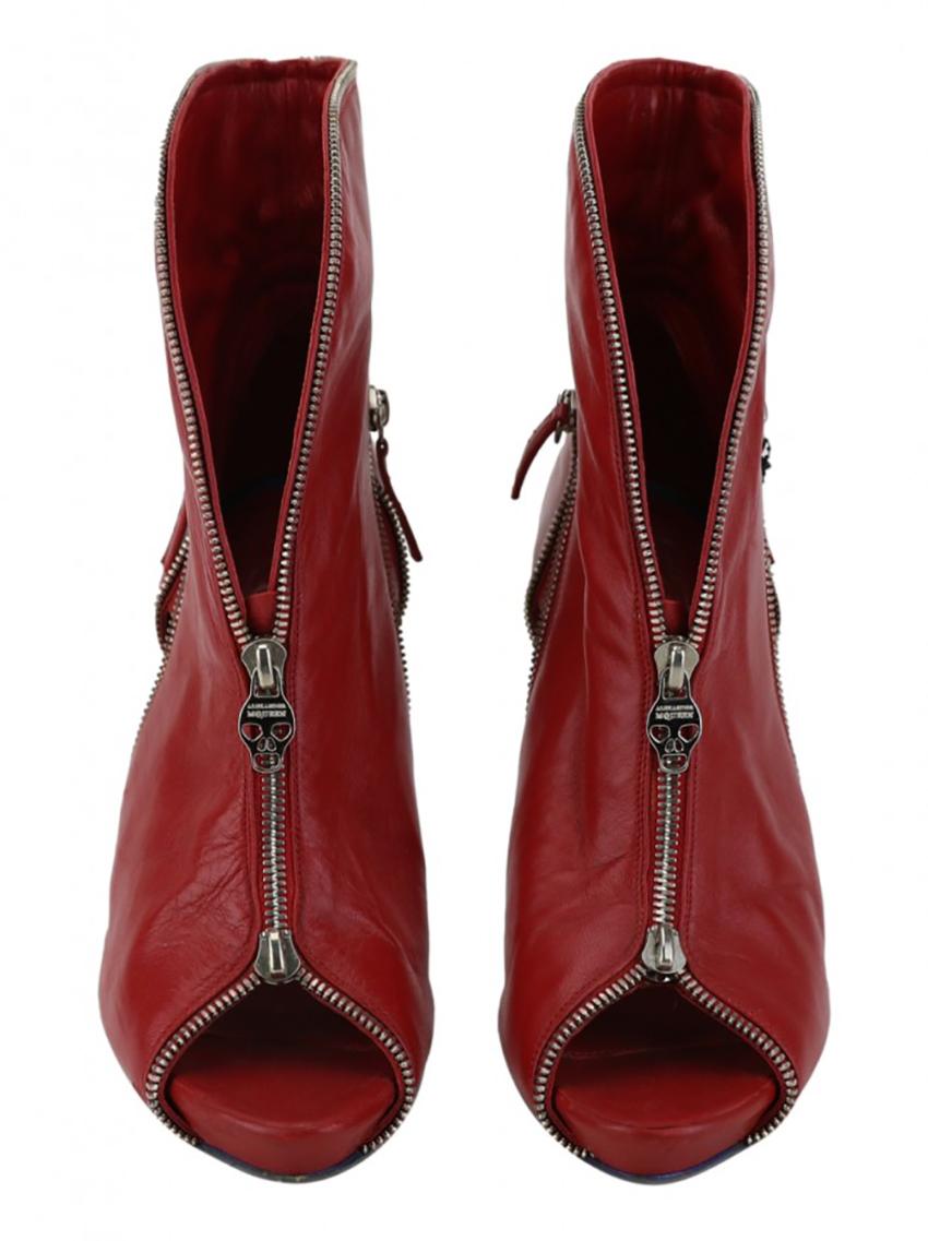 Original Red Alexander McQueen Skull Cut-Out Boot made of leather. The model has a zipper detail, cutout on the sides, peep toe opening, heel with a lined detail on the back and a zipper closure with a handle with the brand symbol on the