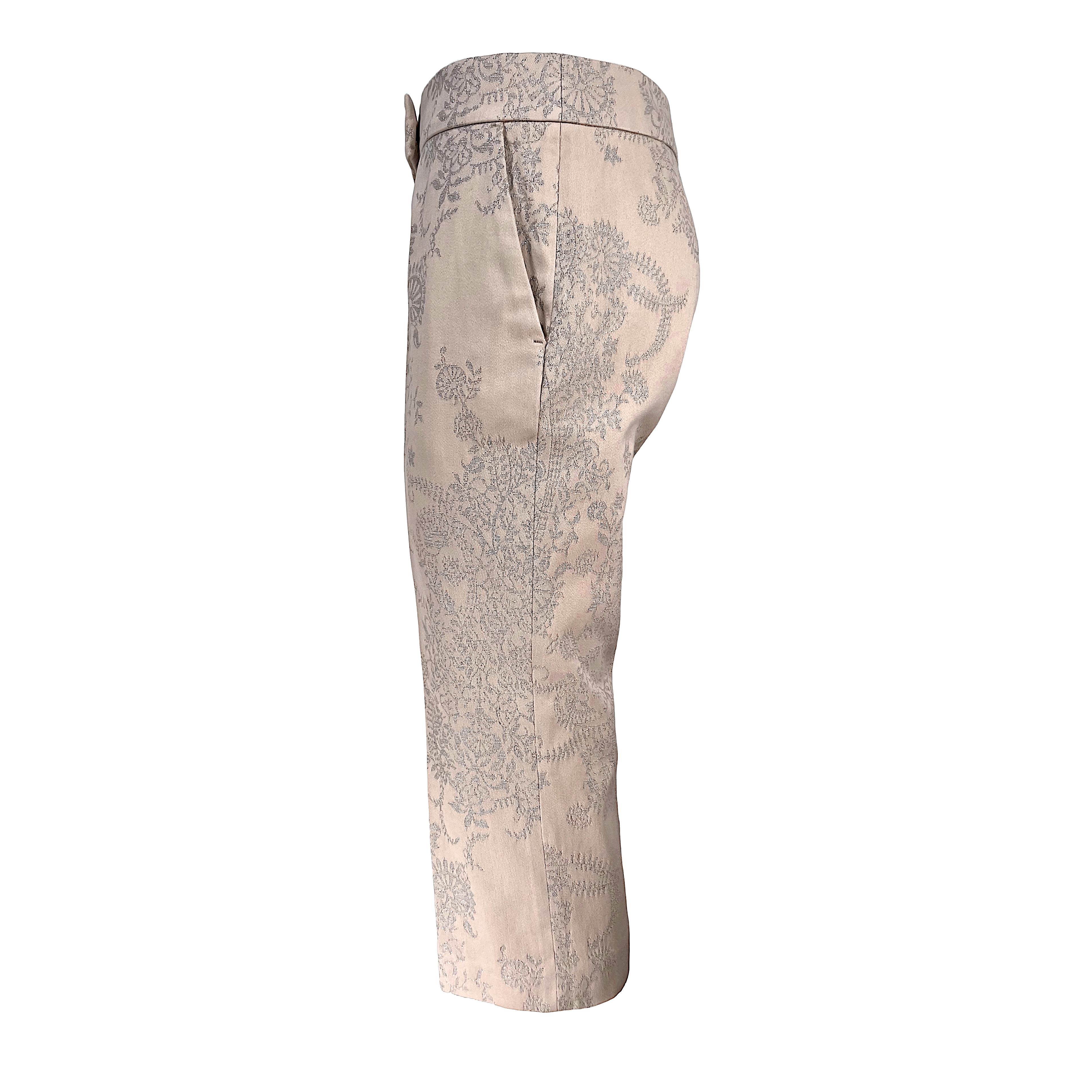 These Vintage Alexander McQueen Capri pants are a stunning addition to your wardrobe. They are crafted from rose-colored cotton jacquard fabric that boasts an intricate silver thread embroidery, creating a luxurious and eye-catching design. The 7/8