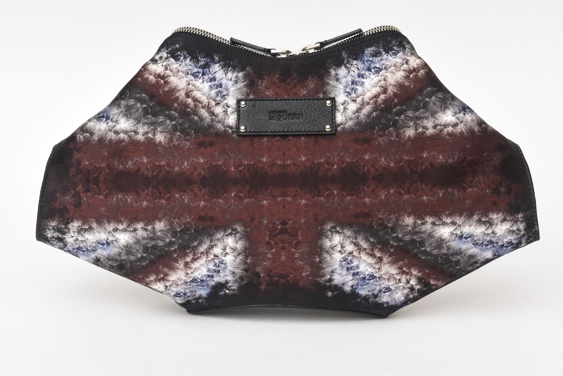 This never used stunning Alexander McQueen De Manta clutch is silk satin with the folded details and magnetic closures with zippered tops. The colors are more dark and moody and the design is suppose to represent the English flag. The other side has