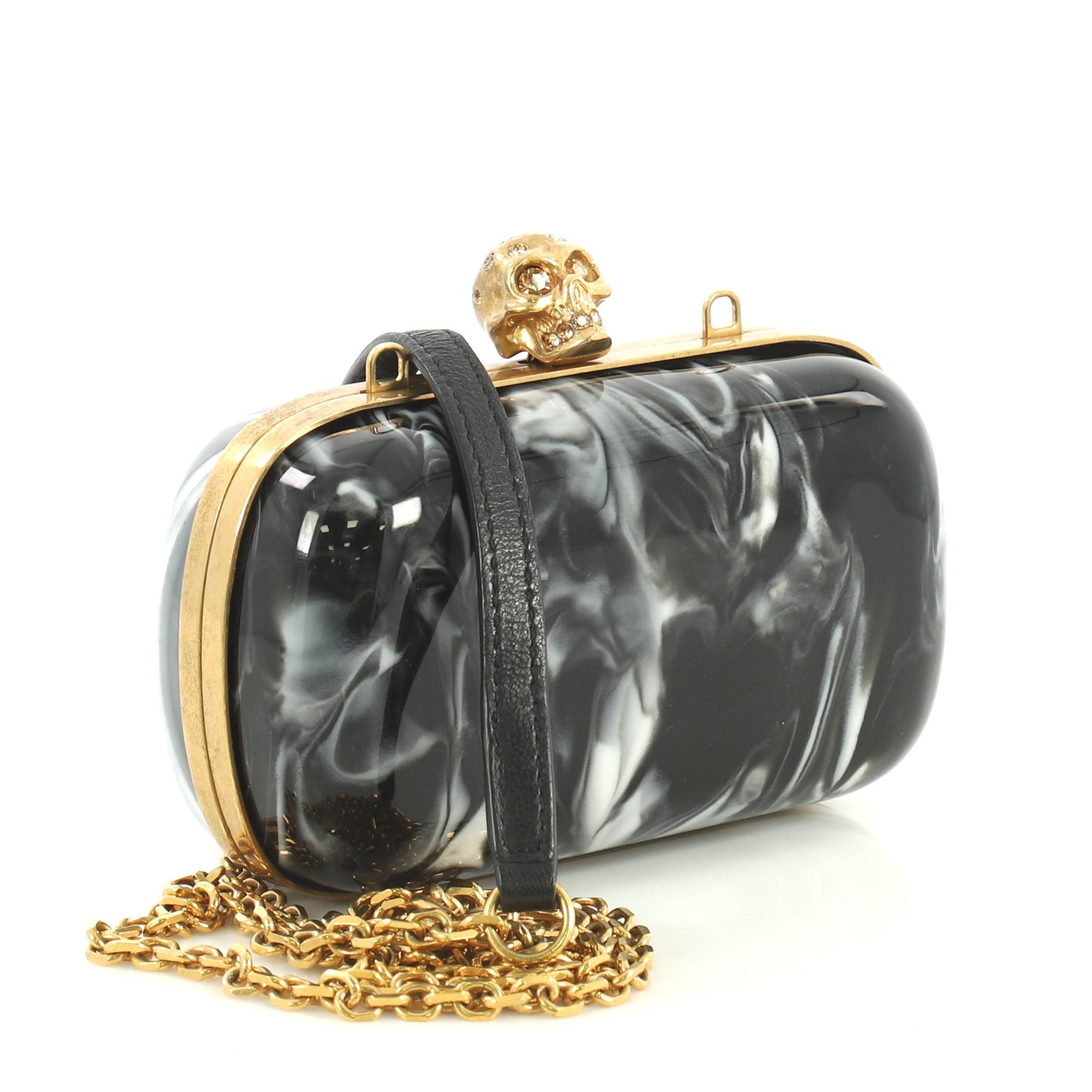This Alexander McQueen Skull Box Clutch Marbled Plexiglass Small, crafted from black plexiglass, features iconic skull clasp with crystal embellishments, hinged metal frame, and aged gold-tone hardware. Its skull clasp closure opens to a black