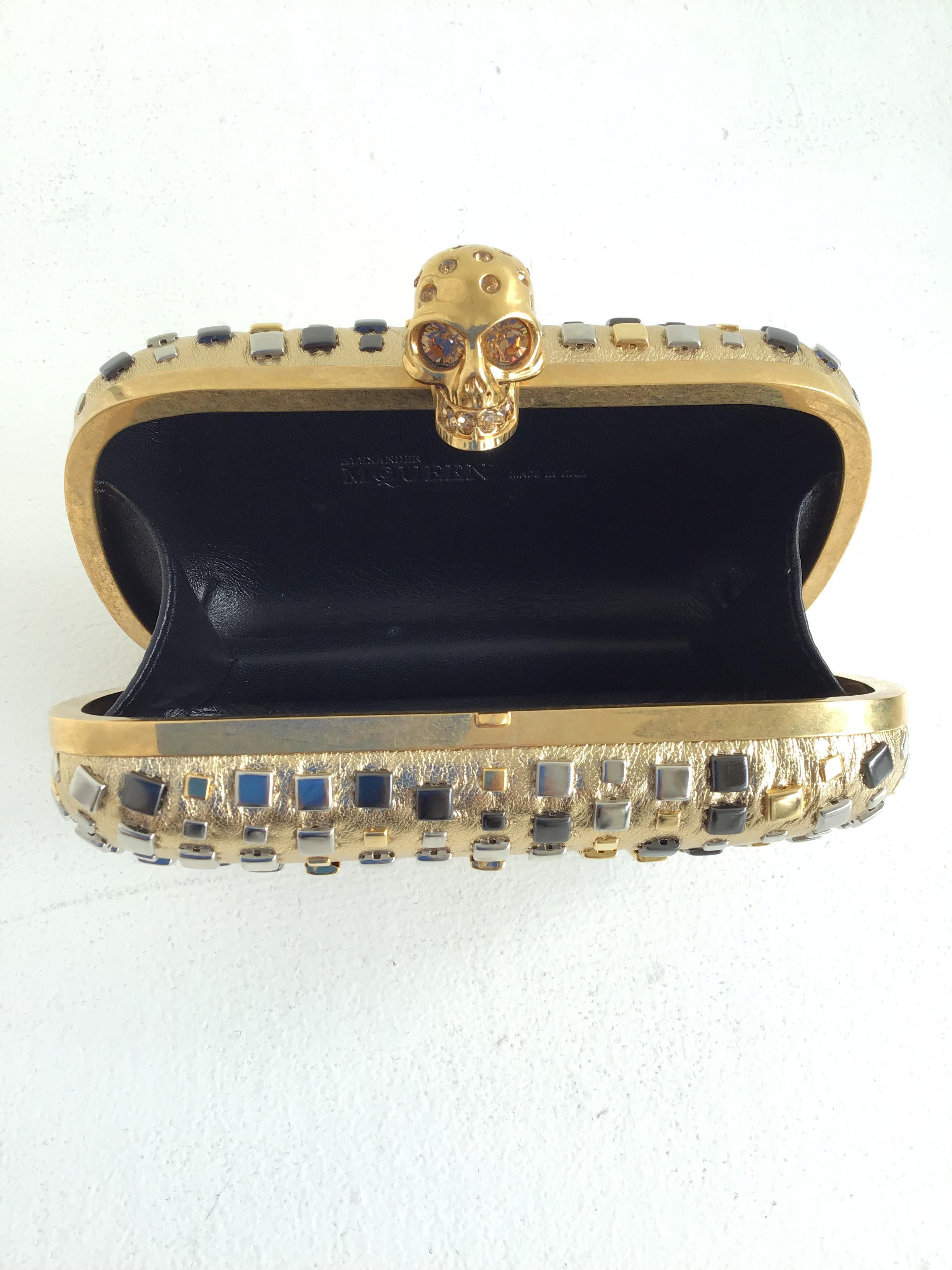 Alexander McQueen Skull Studded Metallic Leather Box Clutch
Description:
Outer Shell: Metallic Gold Lamb Leather with Multicolored Studs 
Gold Jeweled Skull Flip Lock Closure
Inner Shell: Black Leather Lining
