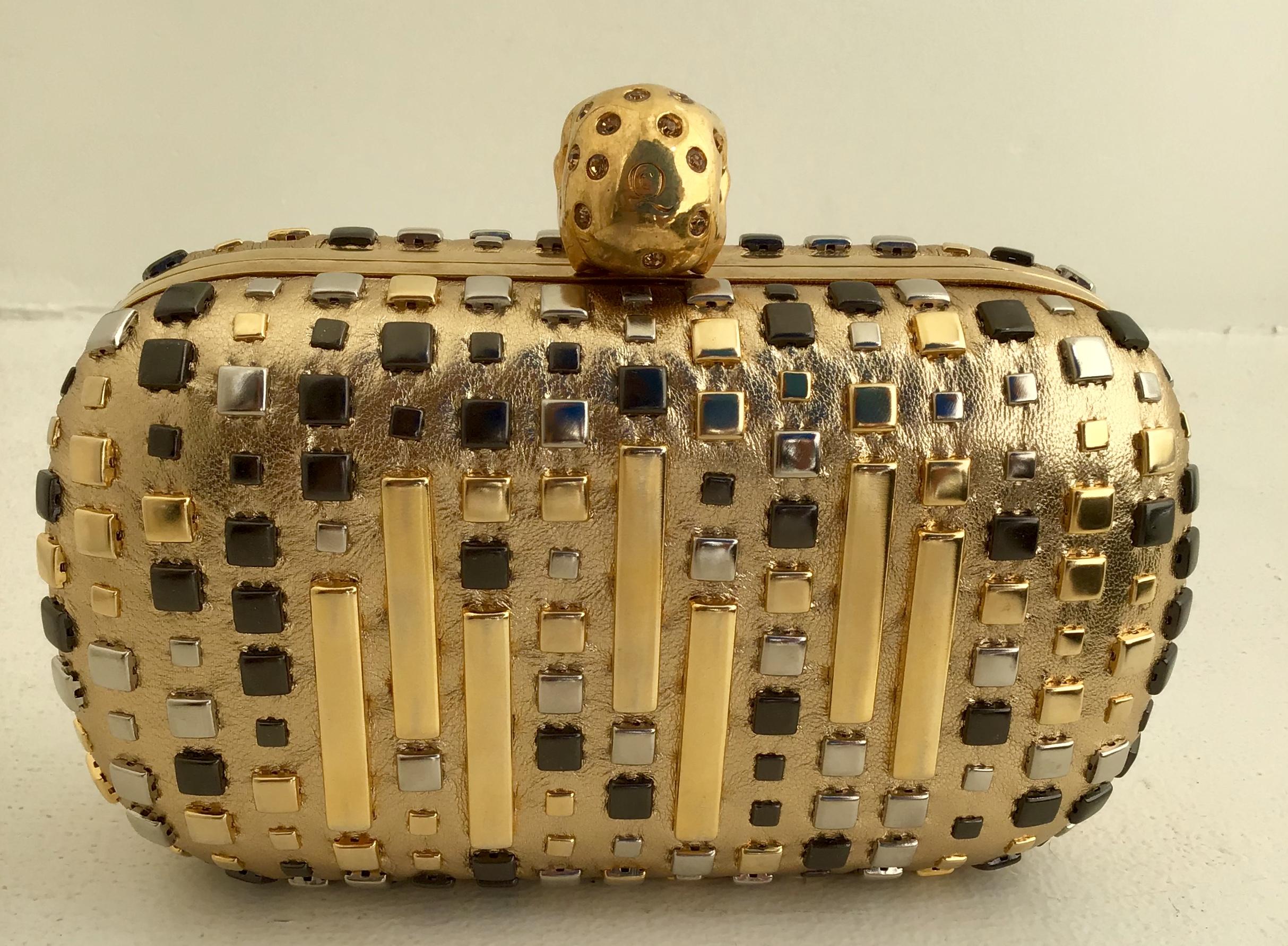 Alexander McQueen Skull Studded Metallic Leather Box Clutch. The outer shell is a metallic gold lamb leather with multicolored studs. Gold jeweled skull flip lock closure. The inner shell has a black leather lining. 