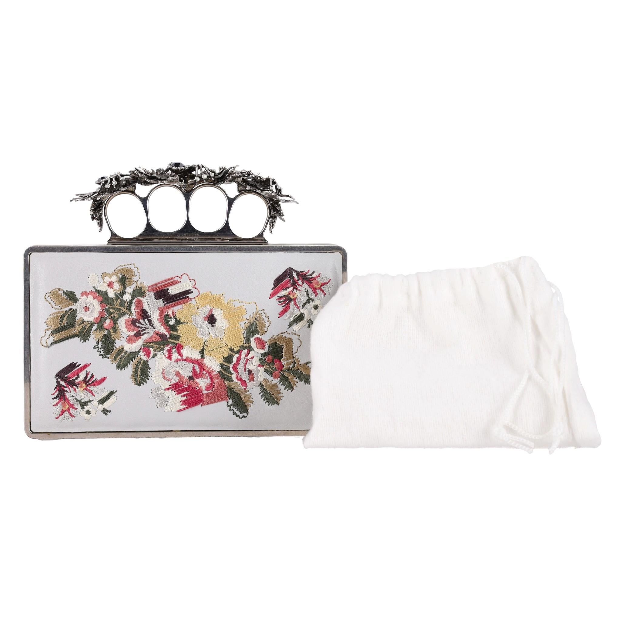 Alexander McQueen - Pochette en cuir brodé de fleurs d'araignée et de crâne

Sac en cuir gris clair avec de magnifiques broderies florales multicolores sur le devant et à l'arrière.

La poignée en argent vieilli, signature de la marque, est ornée