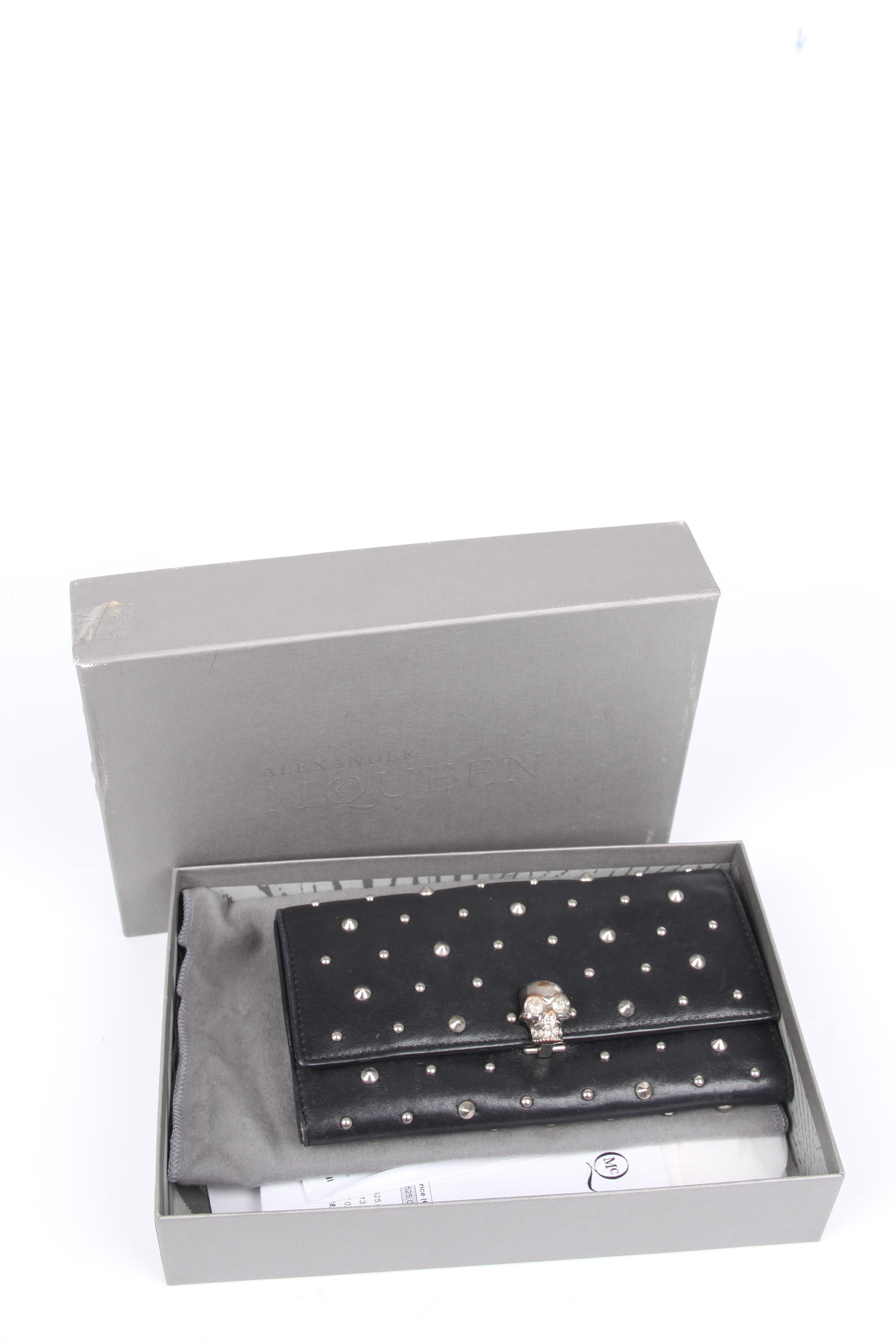 Spacious wallet by Alexander McQueen in black leather covered with studs.

Front closure of course with the welknown skull, this time executed in silver-tone metal. On the back a strap with a push button. Enough space to store 7 credit of debet